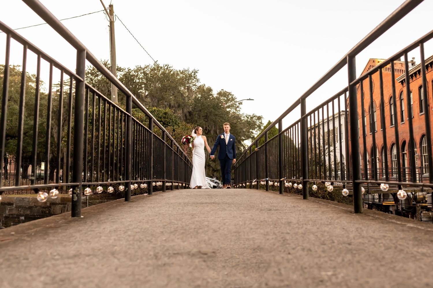 Two figures in wedding attire standing in the distance on a metal bridge walkway creating a romantic silhouette.