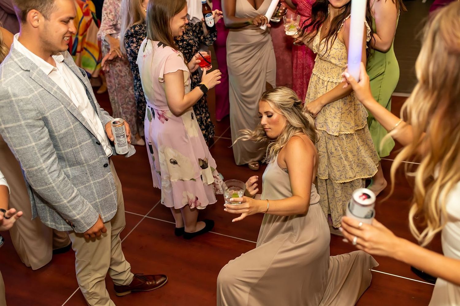 A group of wedding guests dance and socialize on a wooden dance floor during a reception celebration.