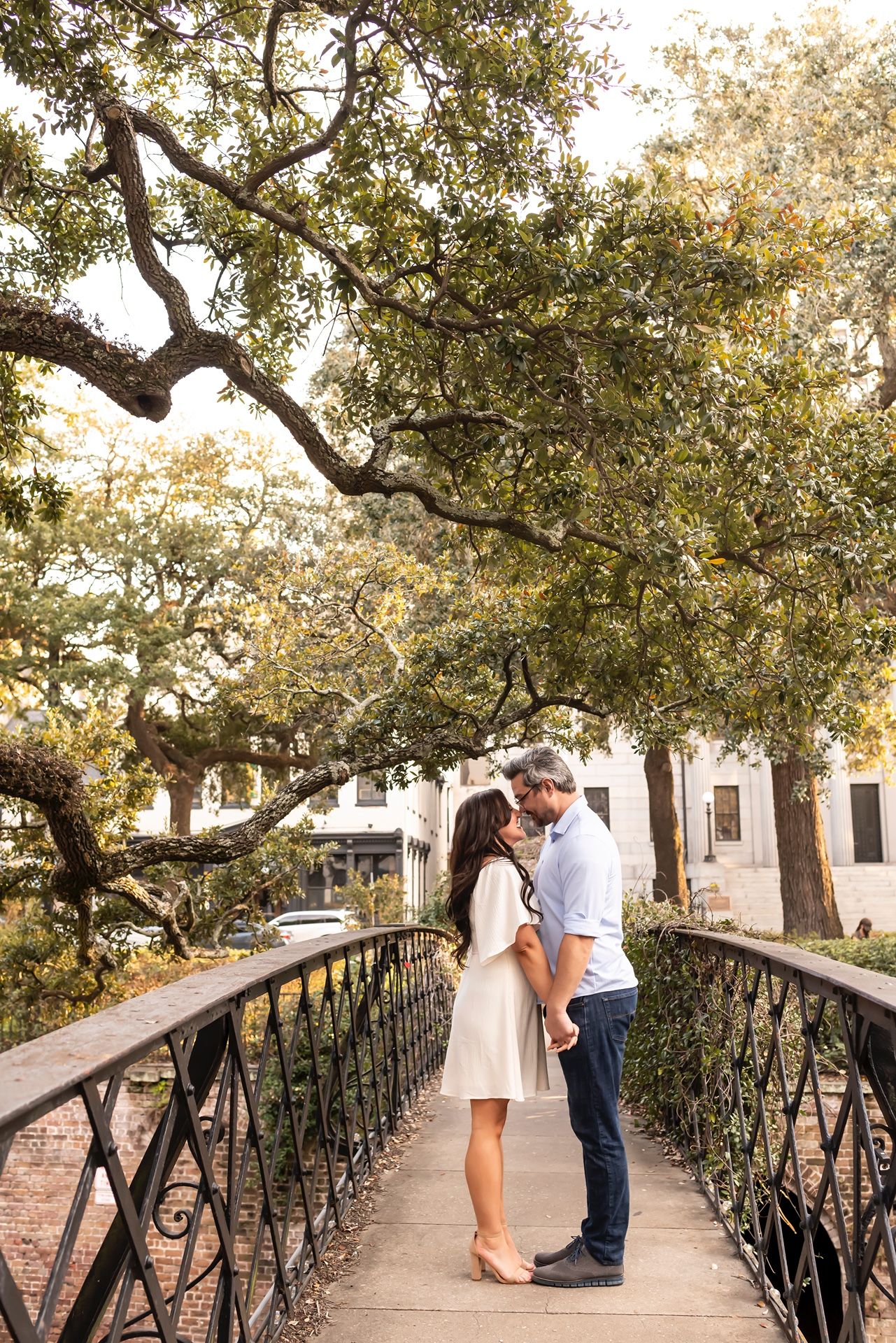 A couple shares a romantic moment on a historic bridge under sprawling oak trees in a charming Southern setting.