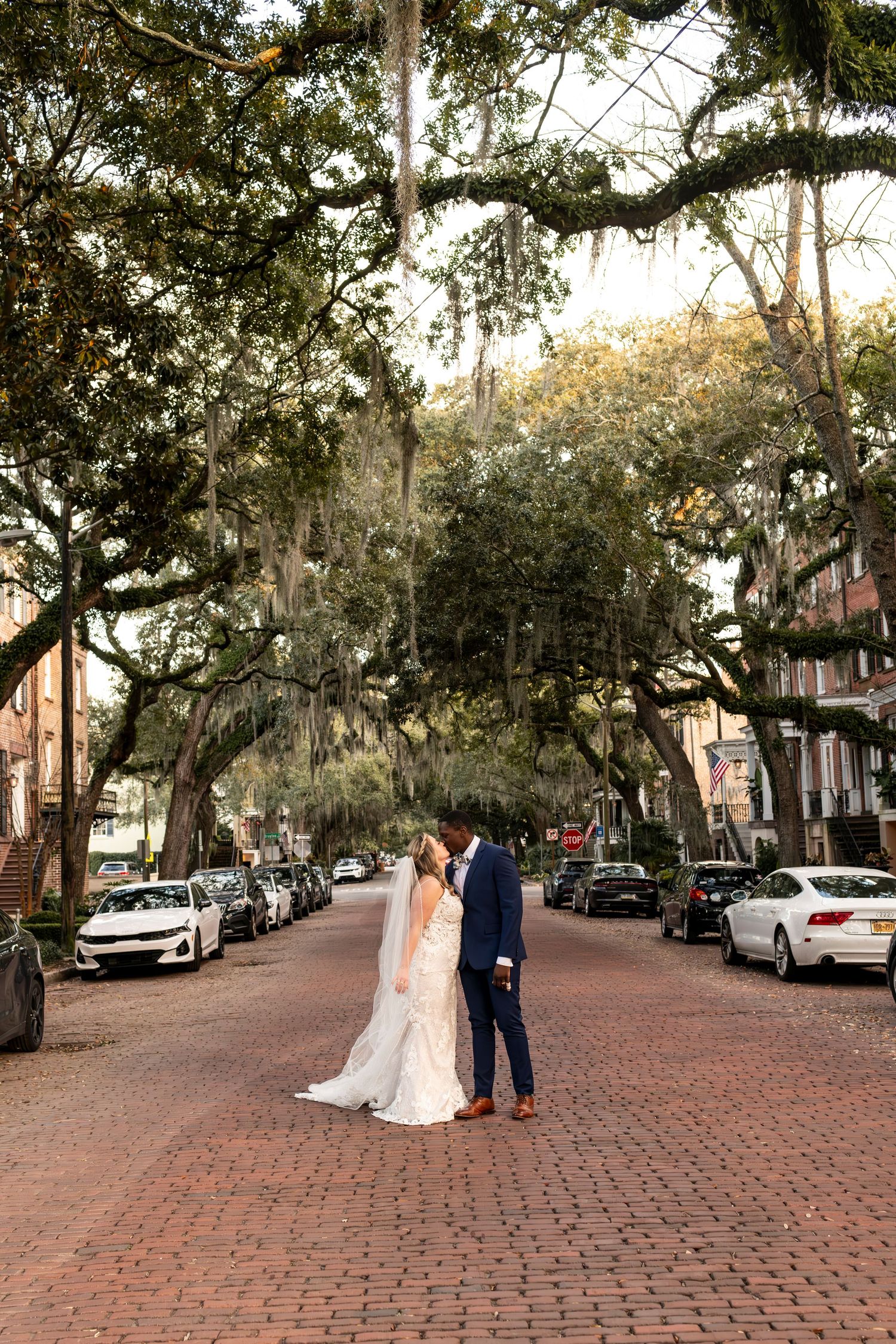 Two people embracing on a romantic brick-paved street lined with Spanish moss-draped oak trees in Savannah, Georgia.