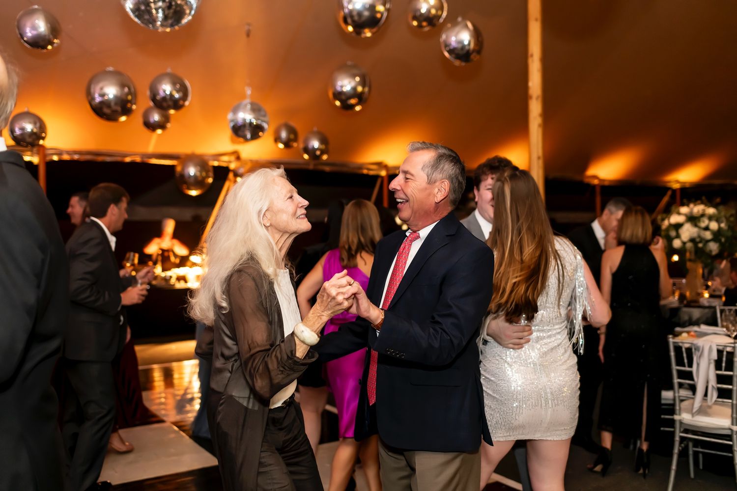 People dancing and socializing under hanging mirror balls during an elegant indoor party celebration.