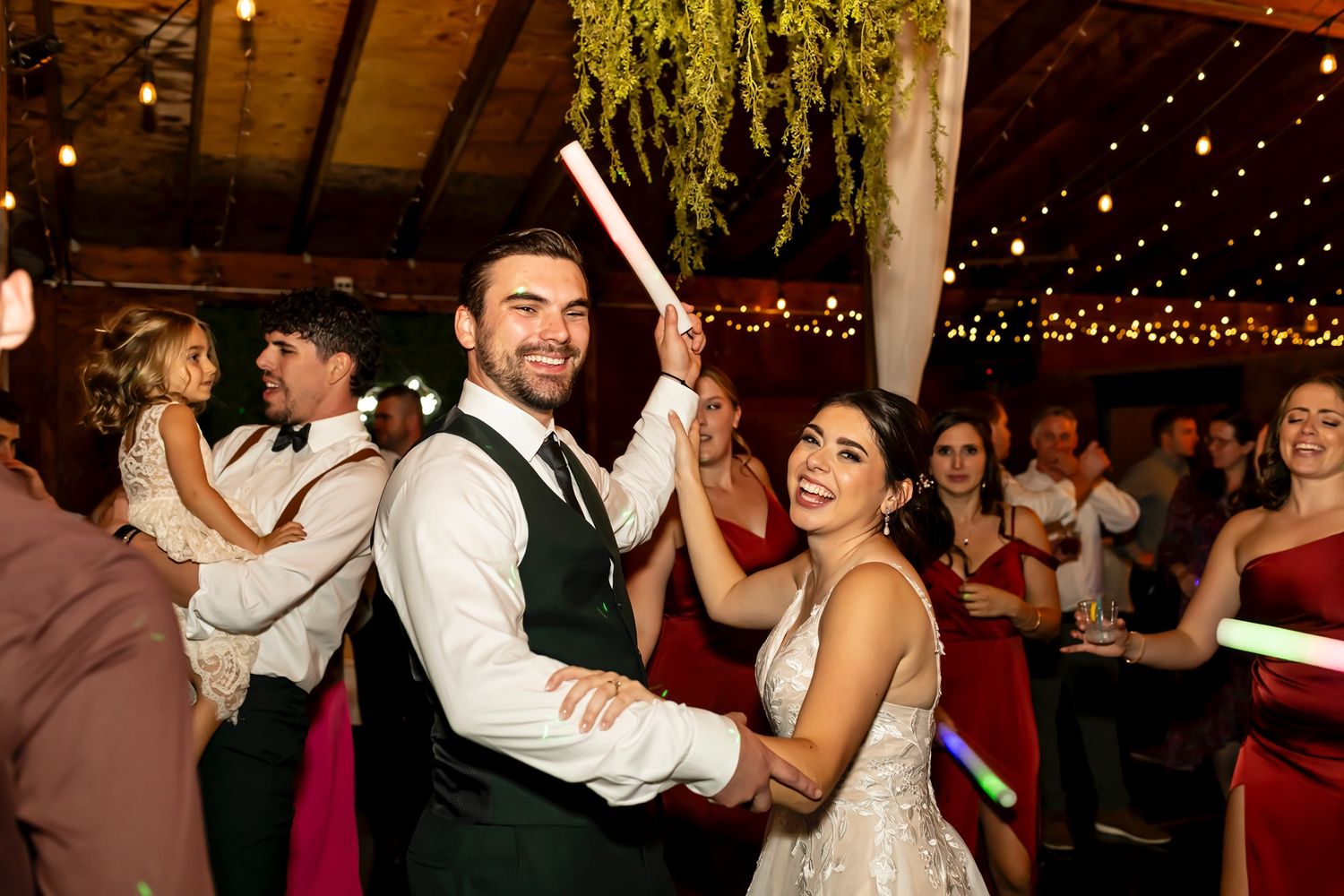 A festive dance floor scene at a wedding reception with guests celebrating under string lights.