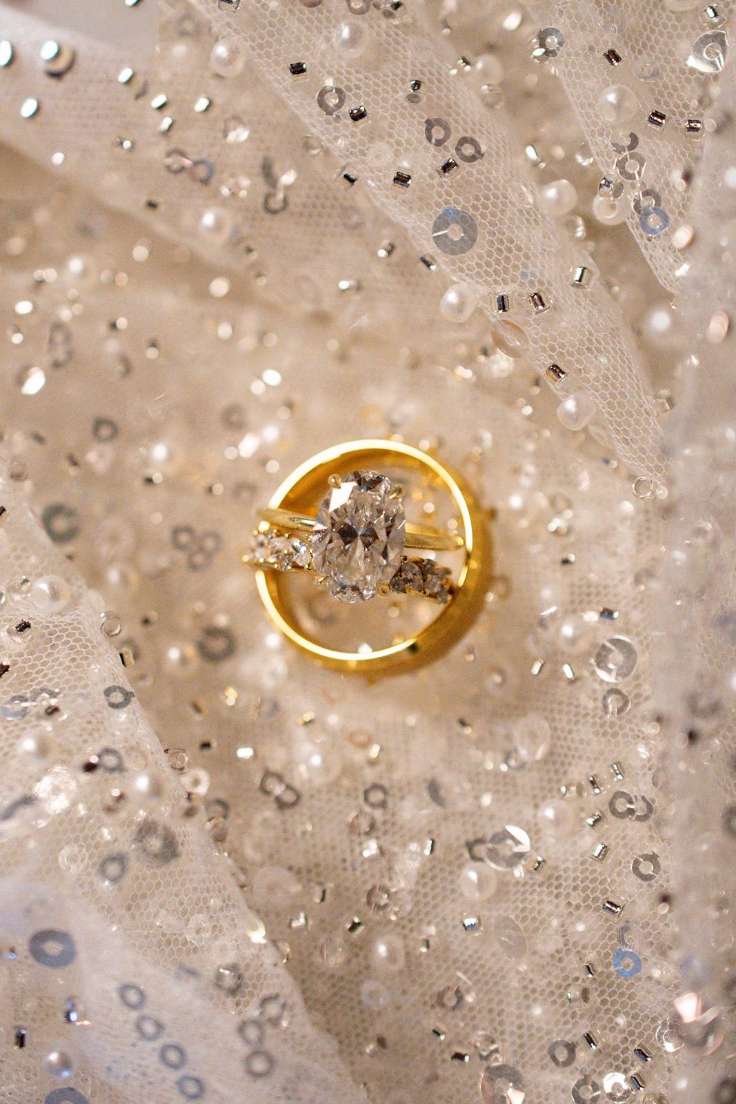 A sparkling diamond engagement ring on gold band photographed against a textured fabric with water droplets.