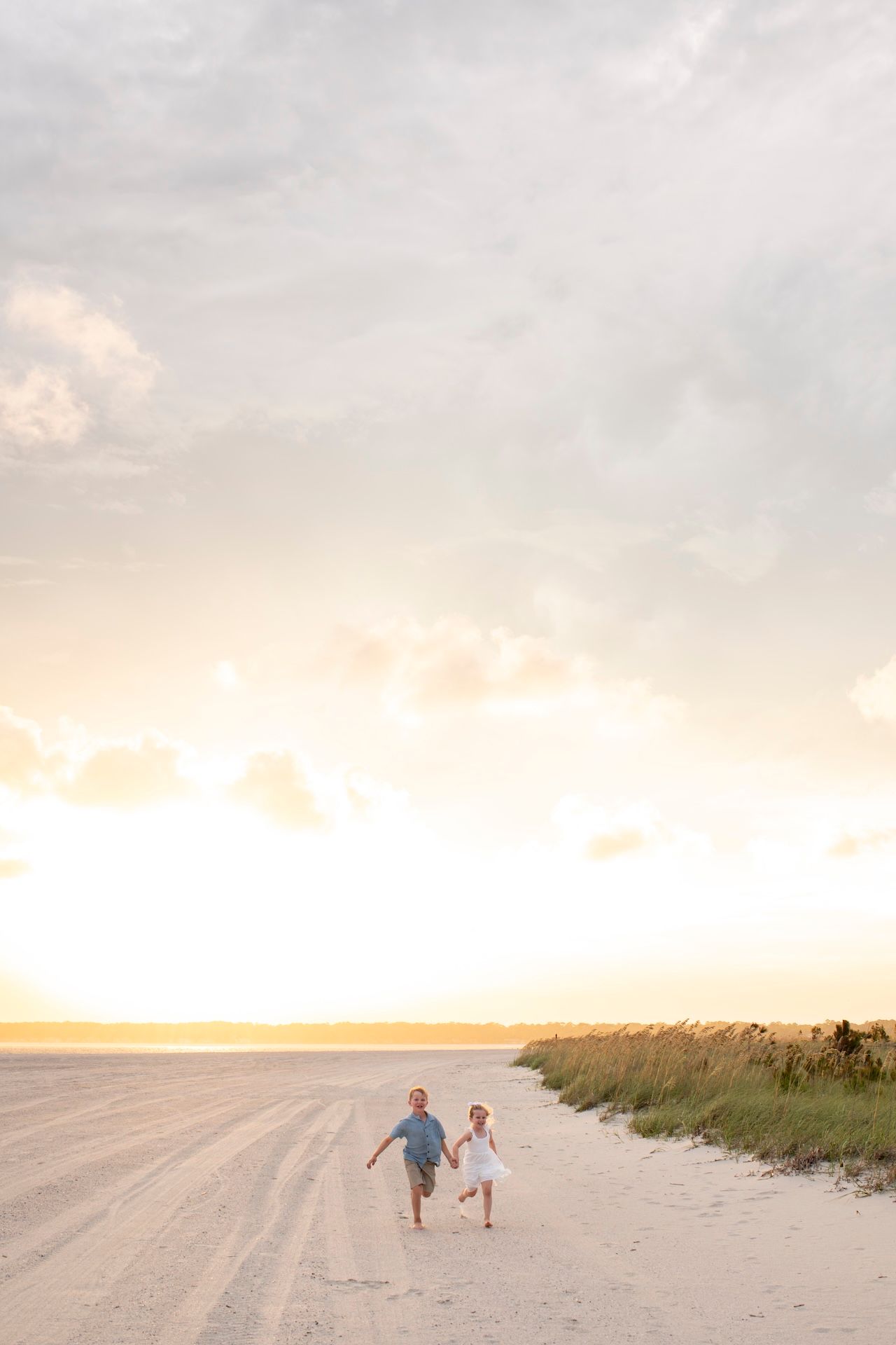 Two children run hand-in-hand along a sandy beach on Hilton Head Island.