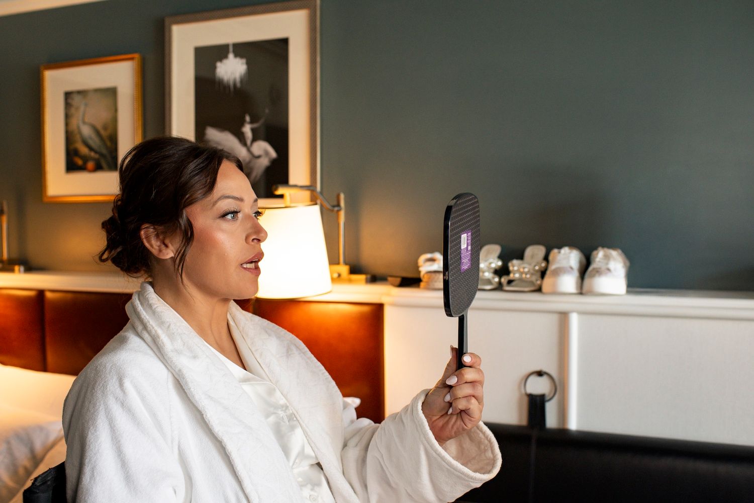 A person wearing a white bathrobe looks at their phone while relaxing in a cozy hotel room with warm lighting.