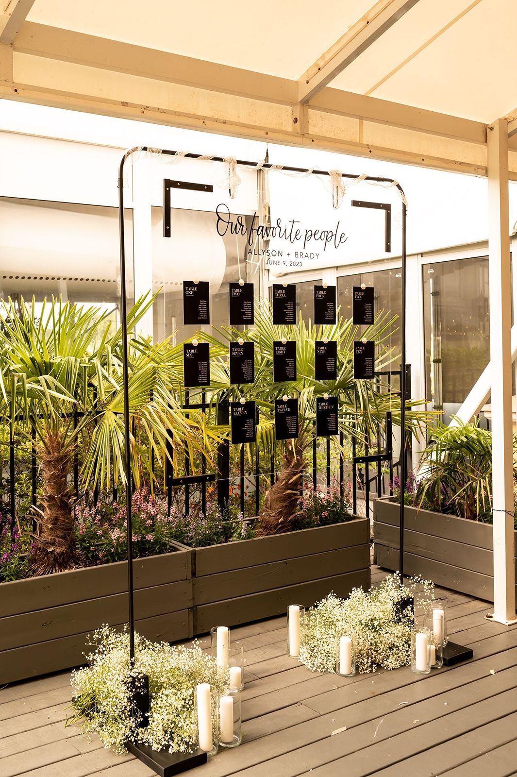 Modern outdoor deck space with wood flooring, white pergola and raised planter boxes filled with tropical plants and palms.