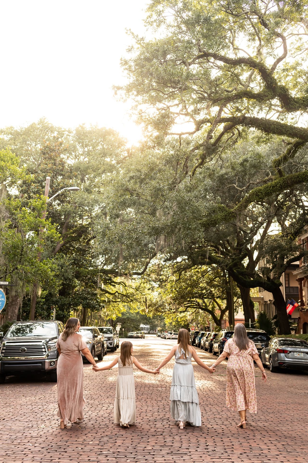 A bridal party walks along a tree-lined brick pathway in downtown Savannah at sunset.