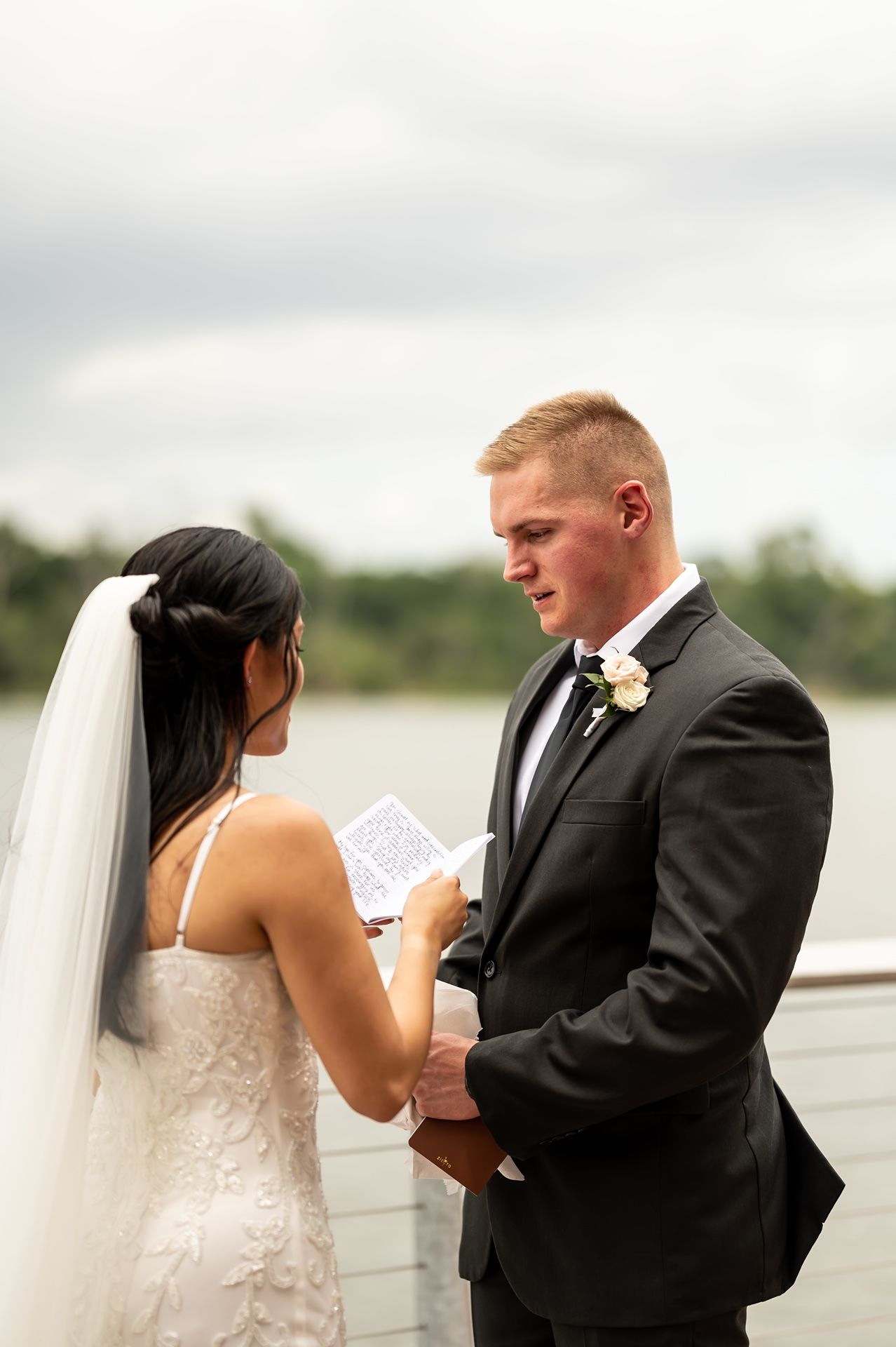 A joyful couple shares an intimate moment on their wedding day along a waterfront boardwalk.