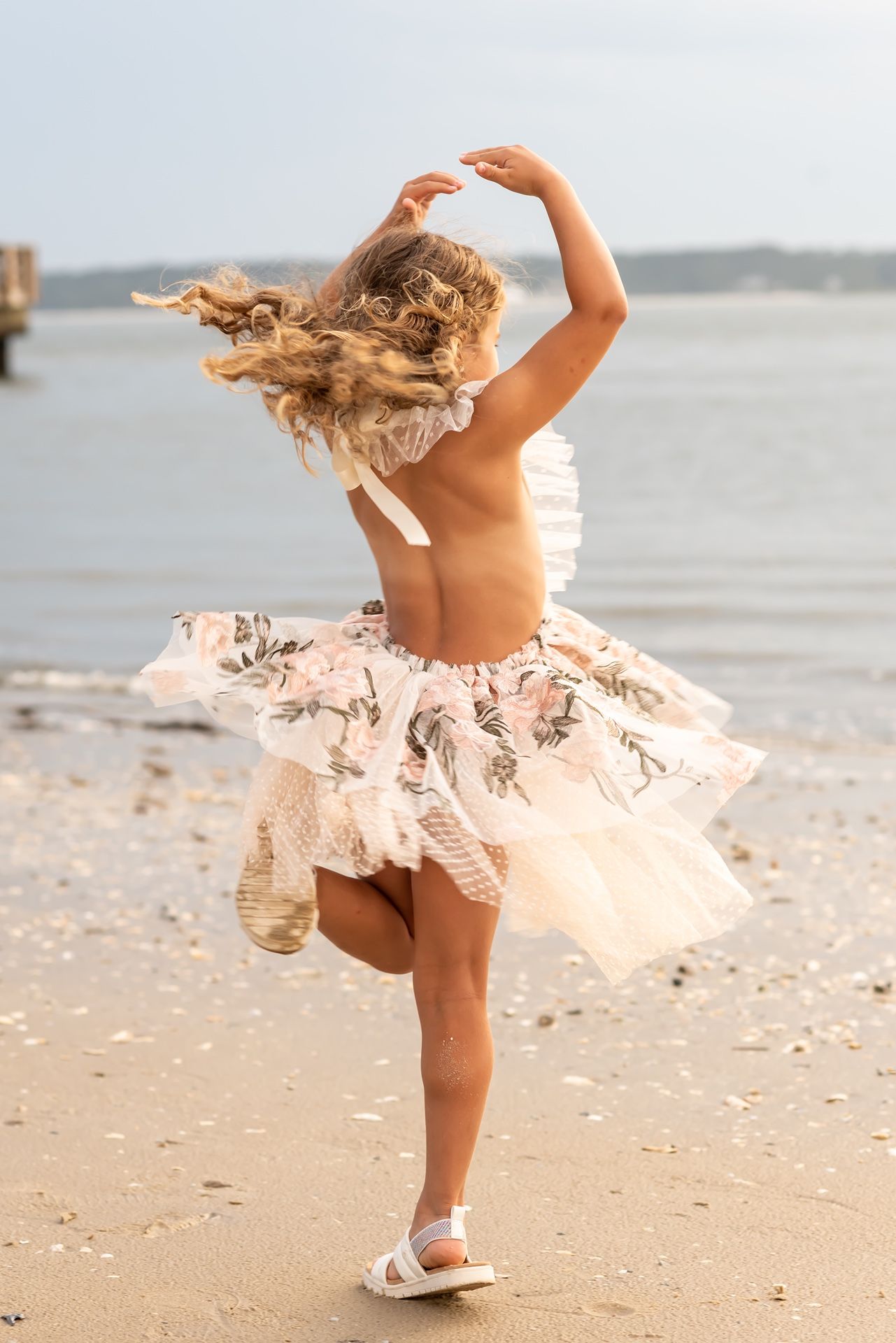 A dancer in a pink tulle skirt twirls gracefully along the sandy beach at sunset.