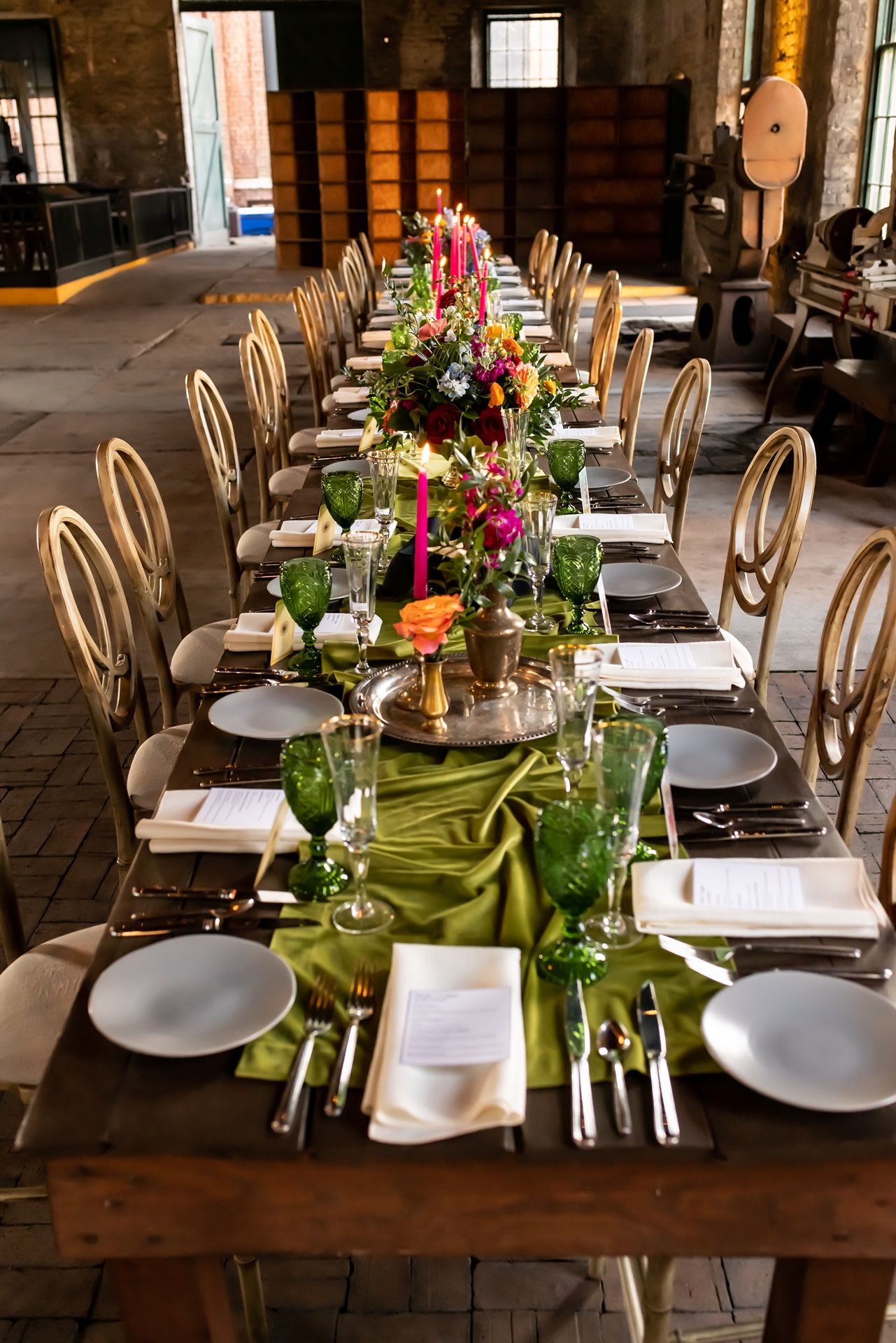 A rustic farmhouse dining table set with white plates, green linens, colorful floral centerpieces and elegant wood chairs.