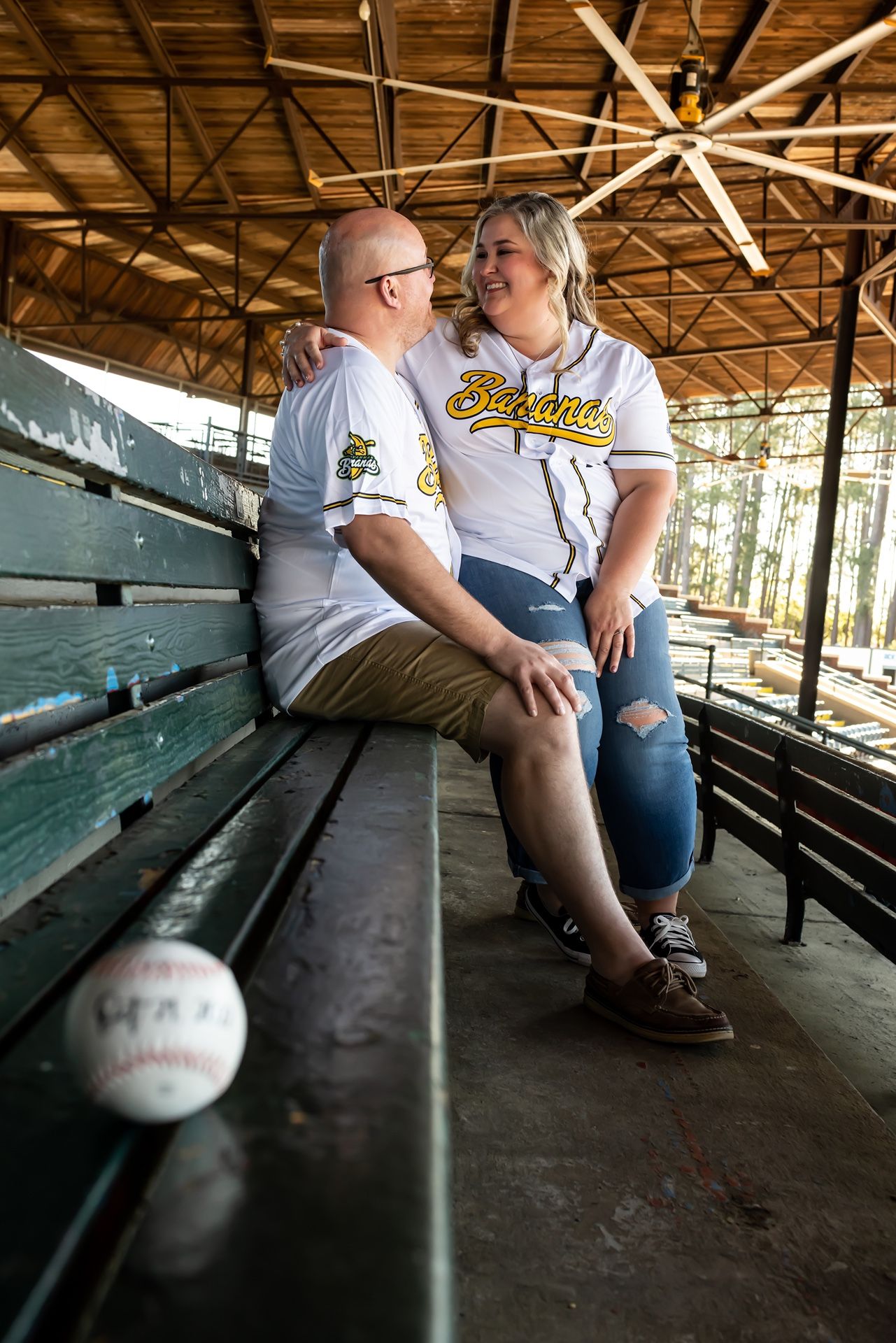 Baseball sits on empty wooden bleachers in an open-air stadium pavilion with rustic lighting and weathered benches.