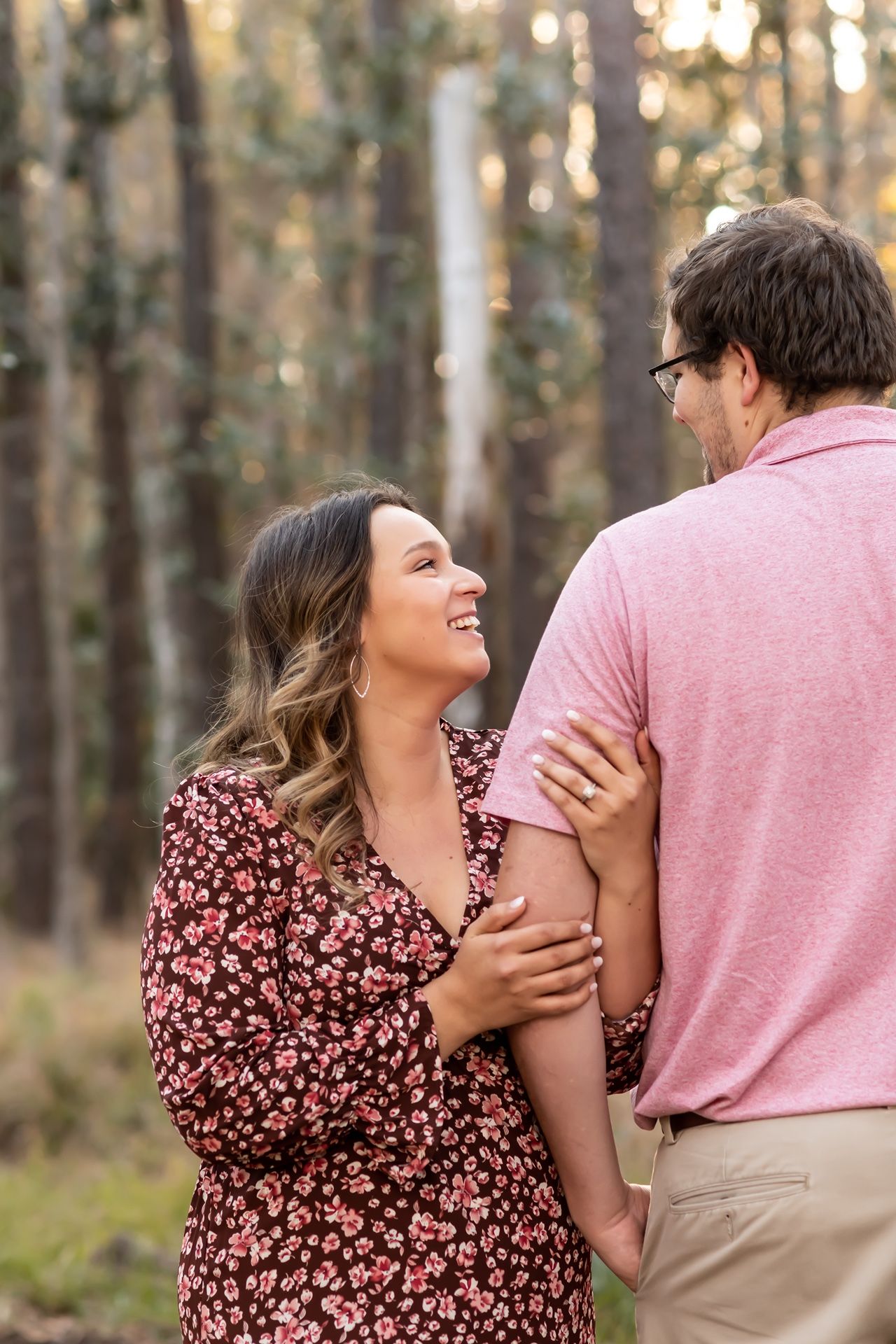 A couple shares a tender moment in a forest setting, with soft bokeh lighting in the background.