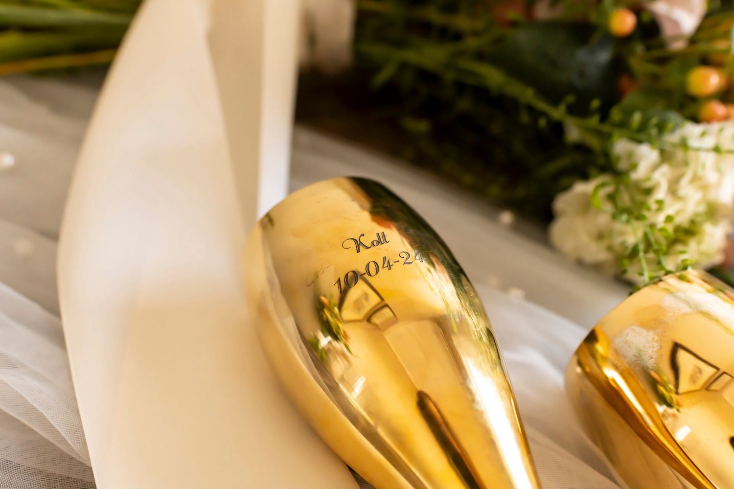 Close-up view of gold champagne bottles with decorative greenery and white ribbon on elegant table setting.