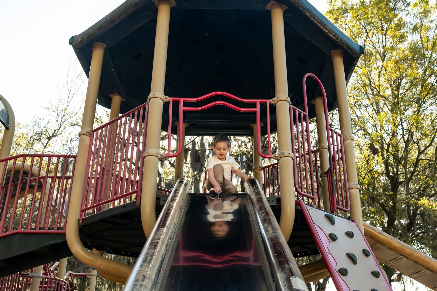 Children playing on a covered playground slide in an outdoor park structure on a sunny autumn day.