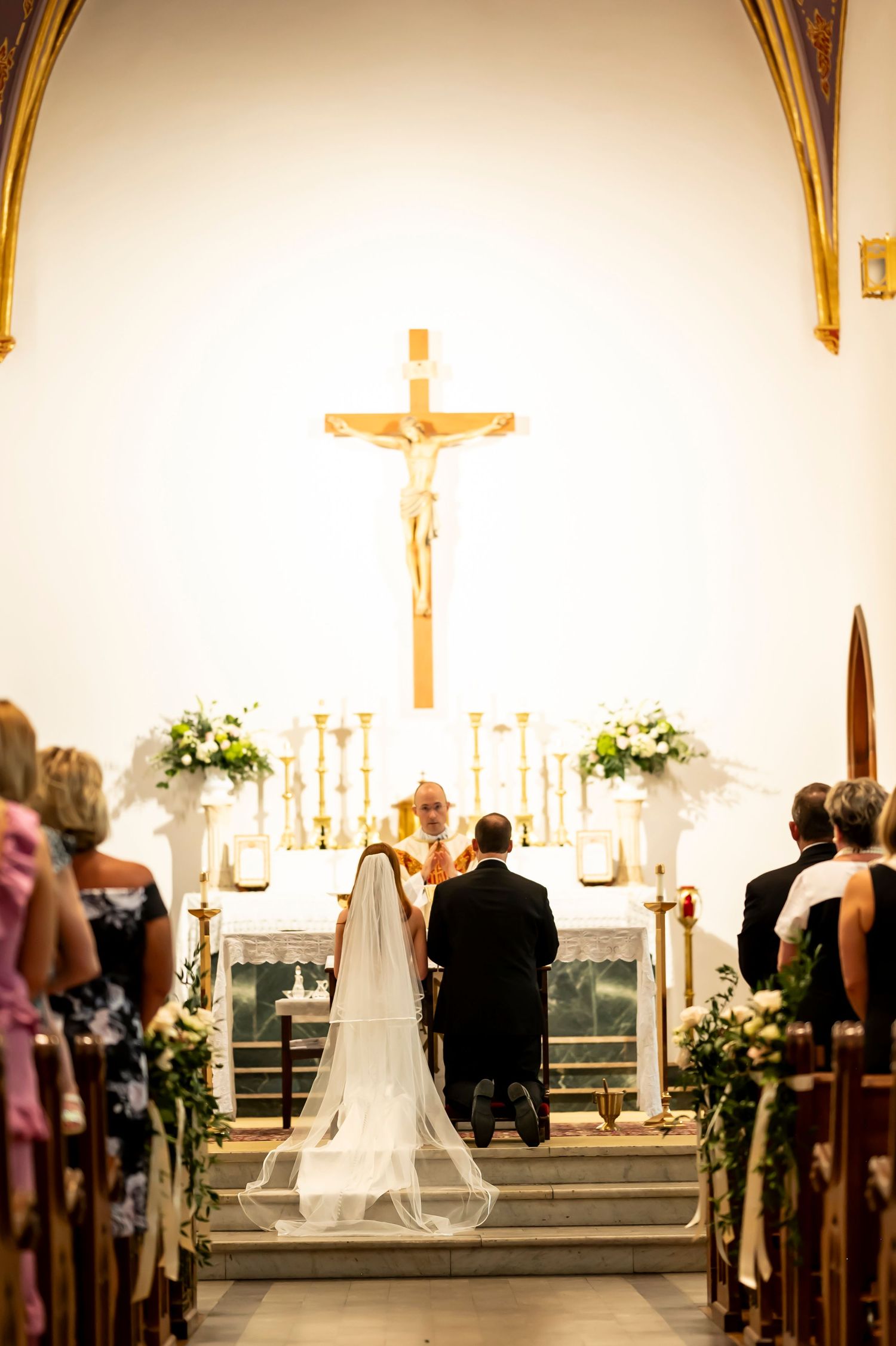 Beautiful church wedding ceremony with candles glowing and floral decorations along the side aisles and altar.