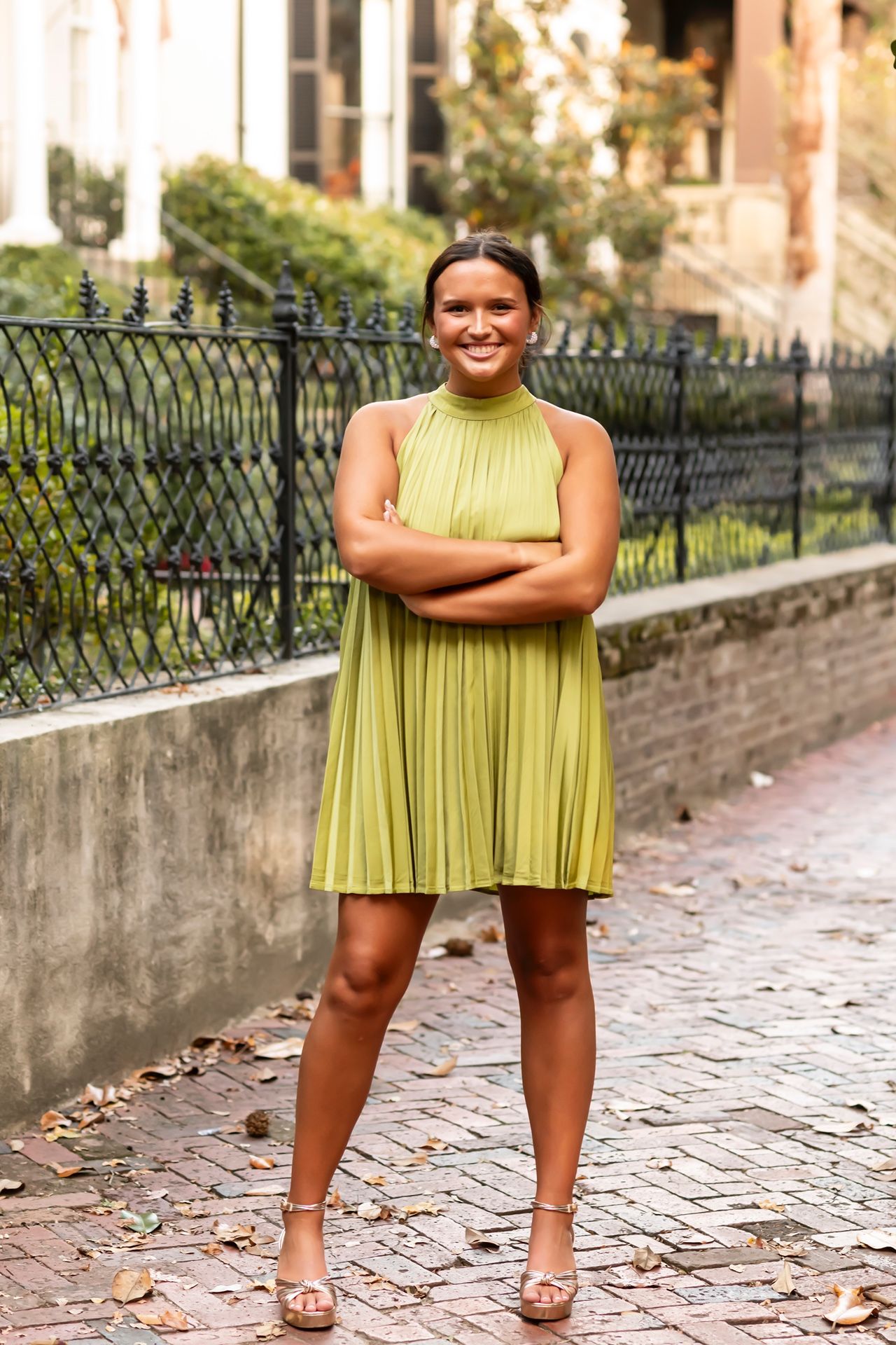 A person wearing a lime green pleated dress poses playfully in multiple shots on a brick-paved walkway.