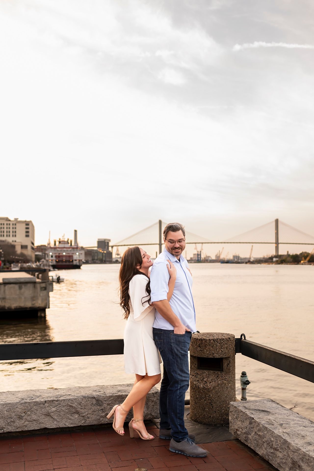 A romantic couple embraces while sitting on a stone wall overlooking the San Francisco Bay and Golden Gate Bridge at sunset.