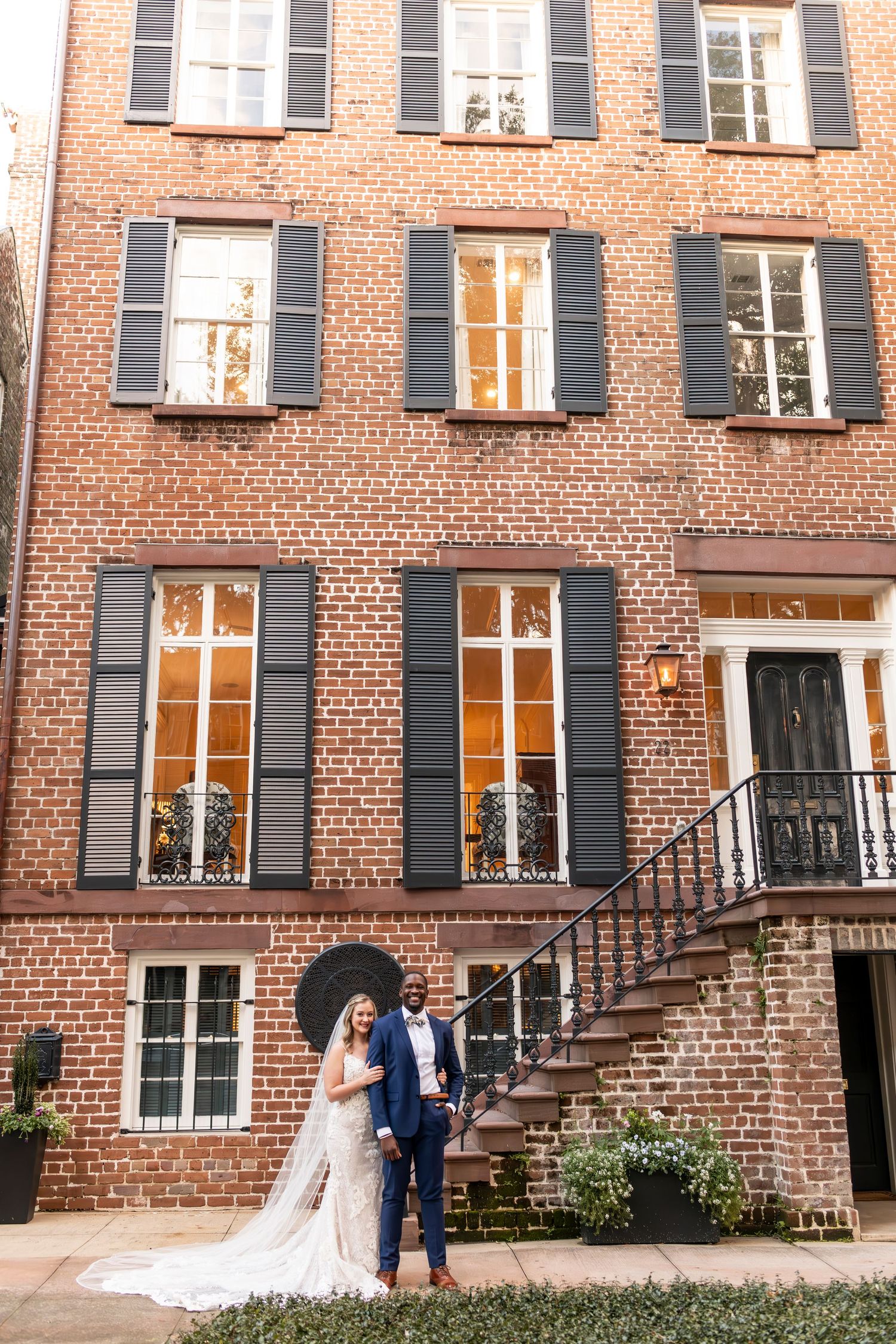 Elegant brick townhouse with black shuttered windows and outdoor staircase showcasing classic Charleston architecture.