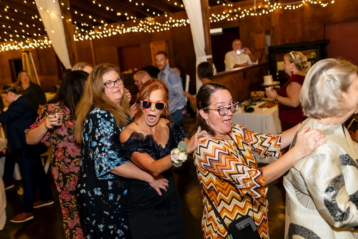 Dance party with string lights overhead as people dance in a rustic venue space.