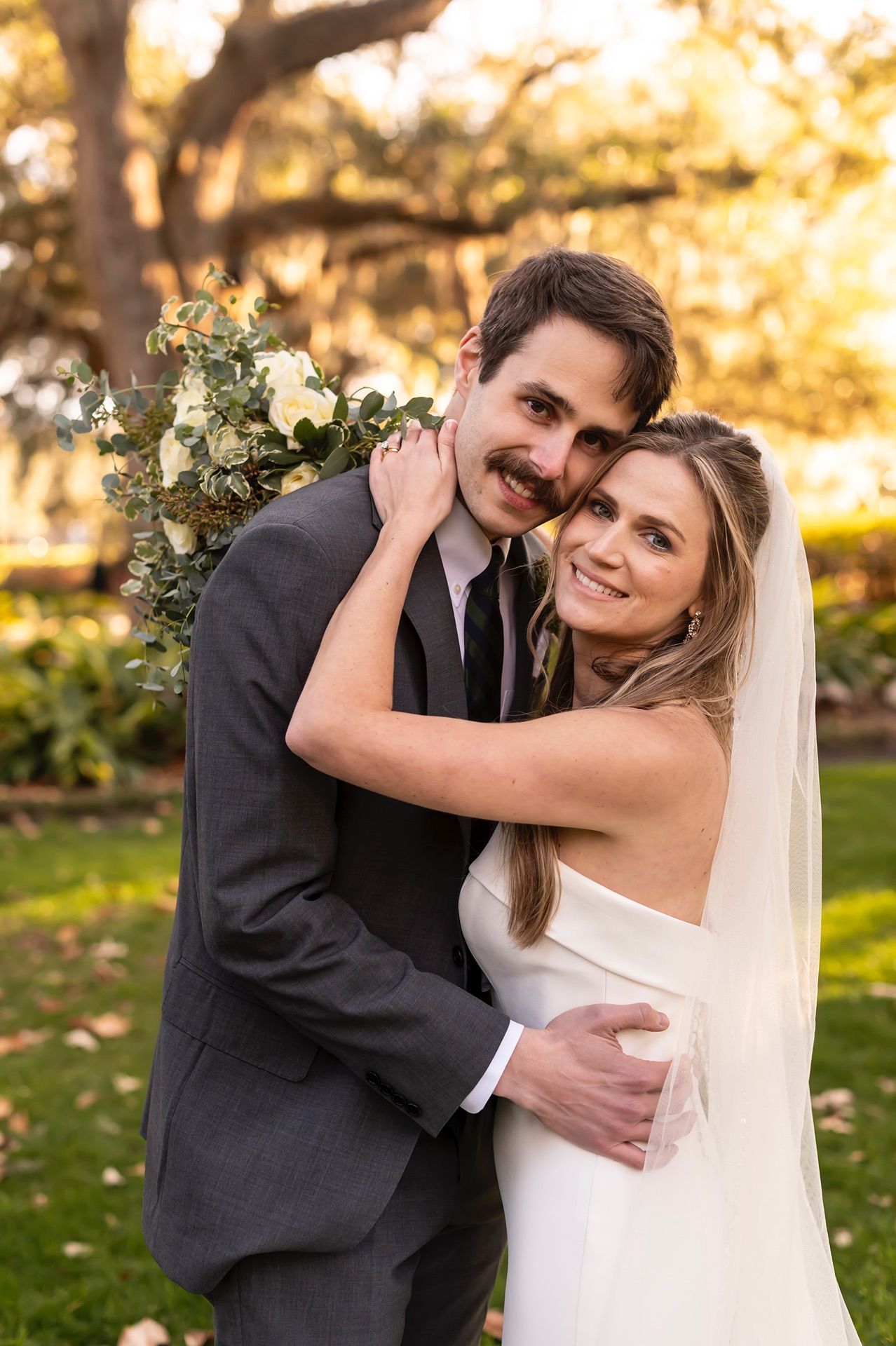 Happy couple embraces outdoors during sunset portrait session in garden setting with warm golden lighting.