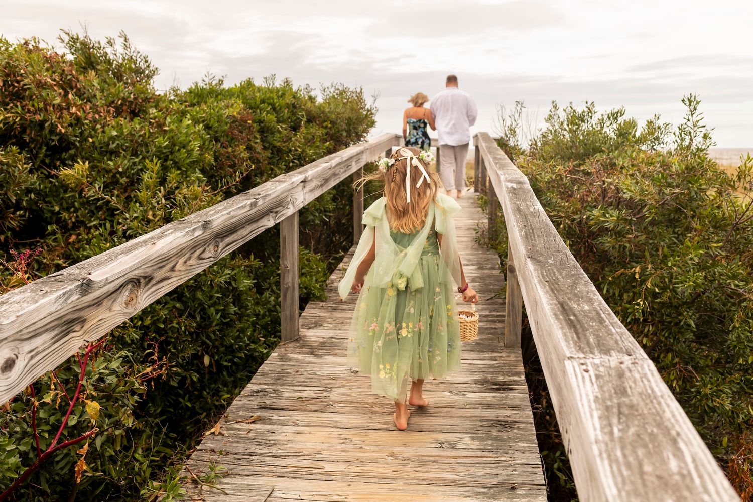 A wooden boardwalk stretches over coastal vegetation with people walking across on a cloudy summer day.
