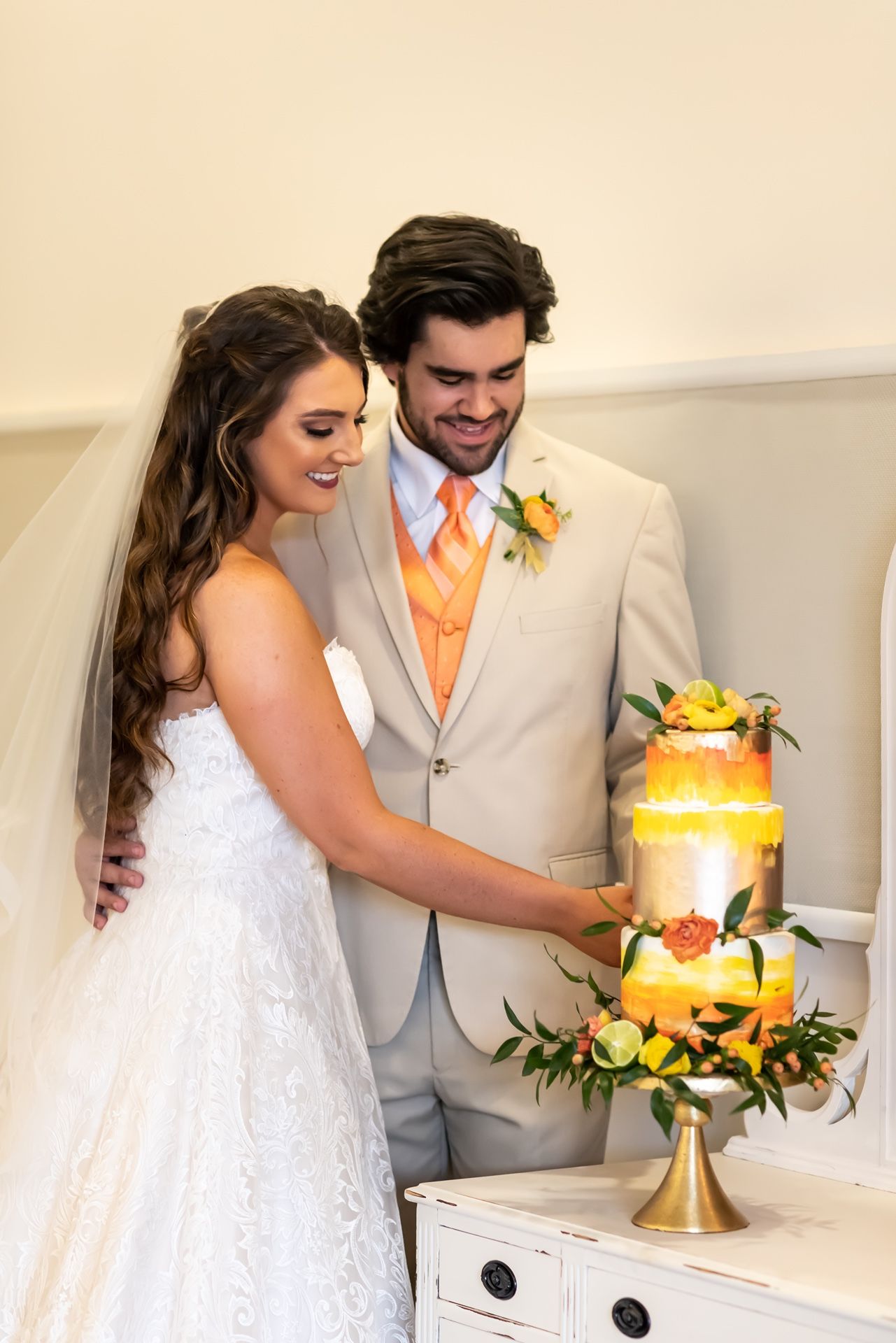 A wedding couple cuts into their three-tiered gold and white cake together at their reception.