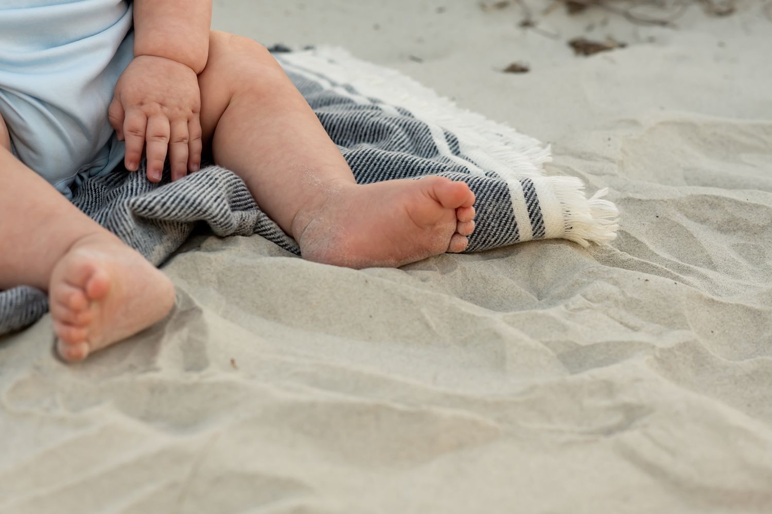 Baby's bare feet resting on a soft blanket atop sandy beach surface.