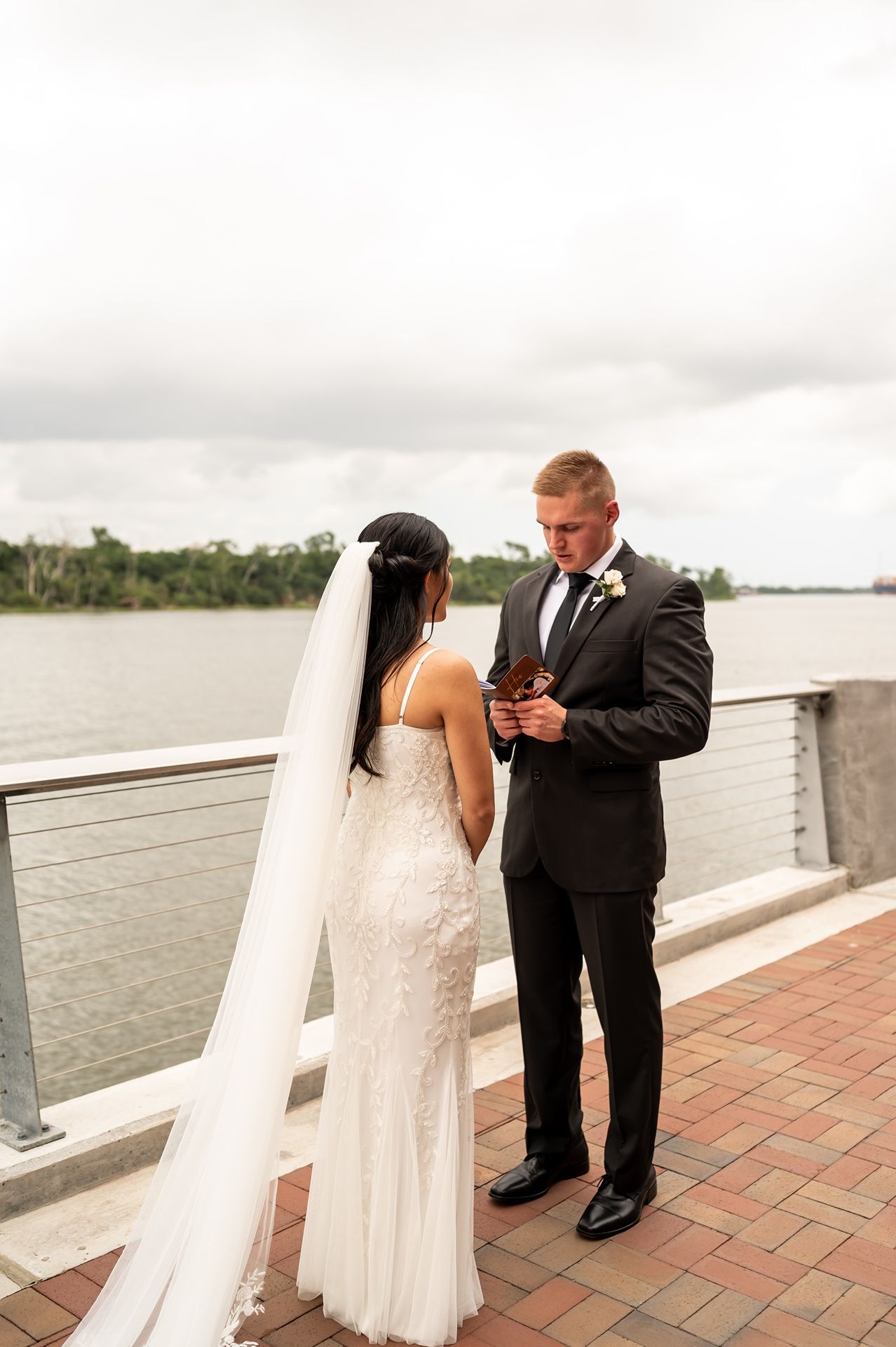 A couple shares an intimate moment during their waterfront wedding ceremony as they exchange vows on a brick patio.