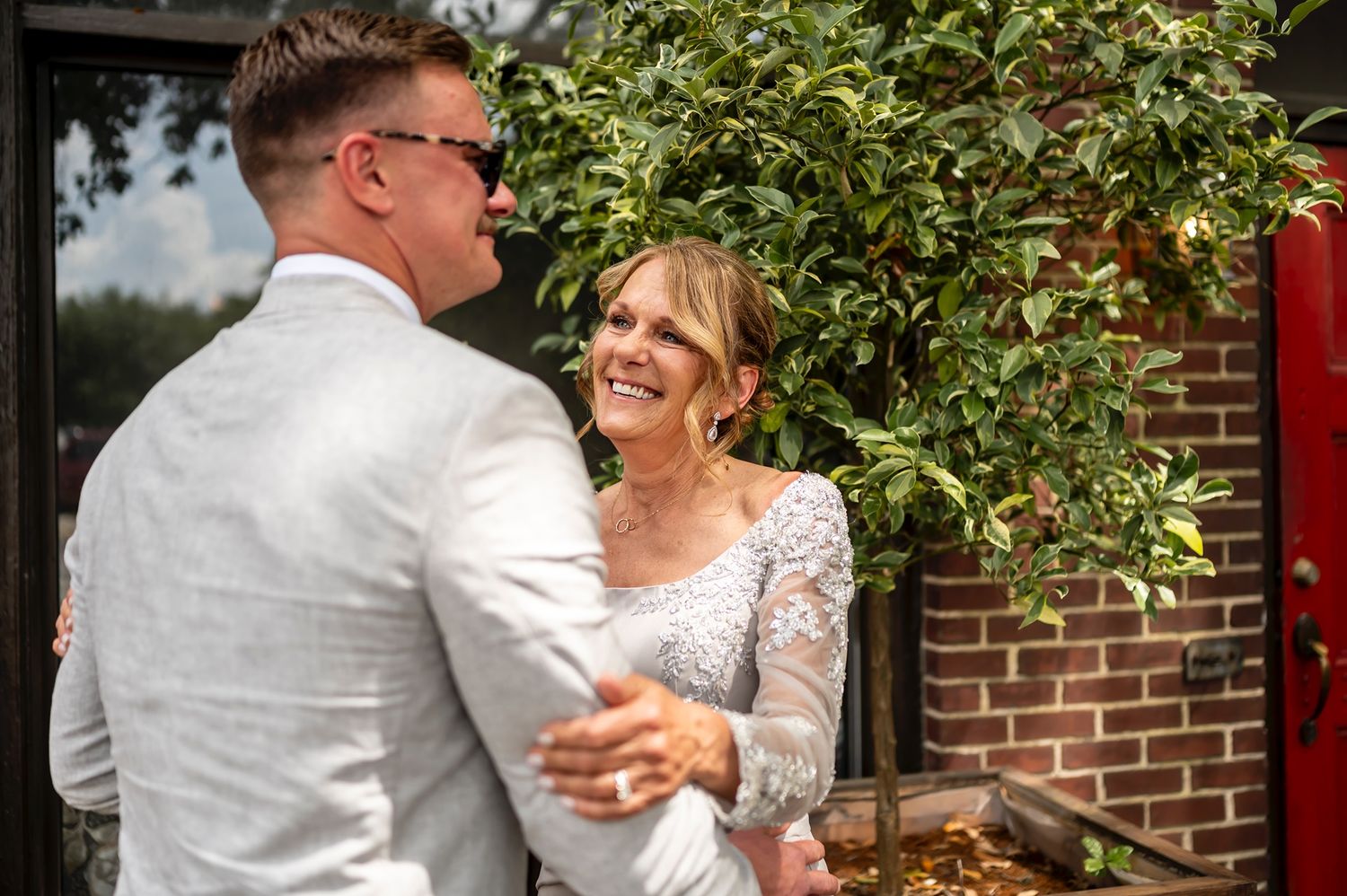 Wedding couple sharing a tender dance outdoors surrounded by greenery and red brick walls.