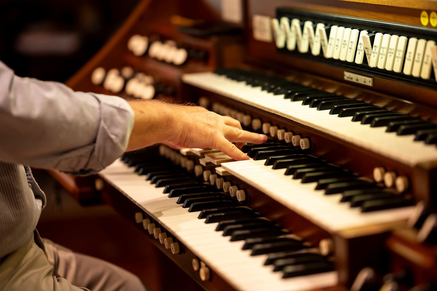A musician's hands playing a vintage organ keyboard with multiple rows of black and white keys in warm lighting.