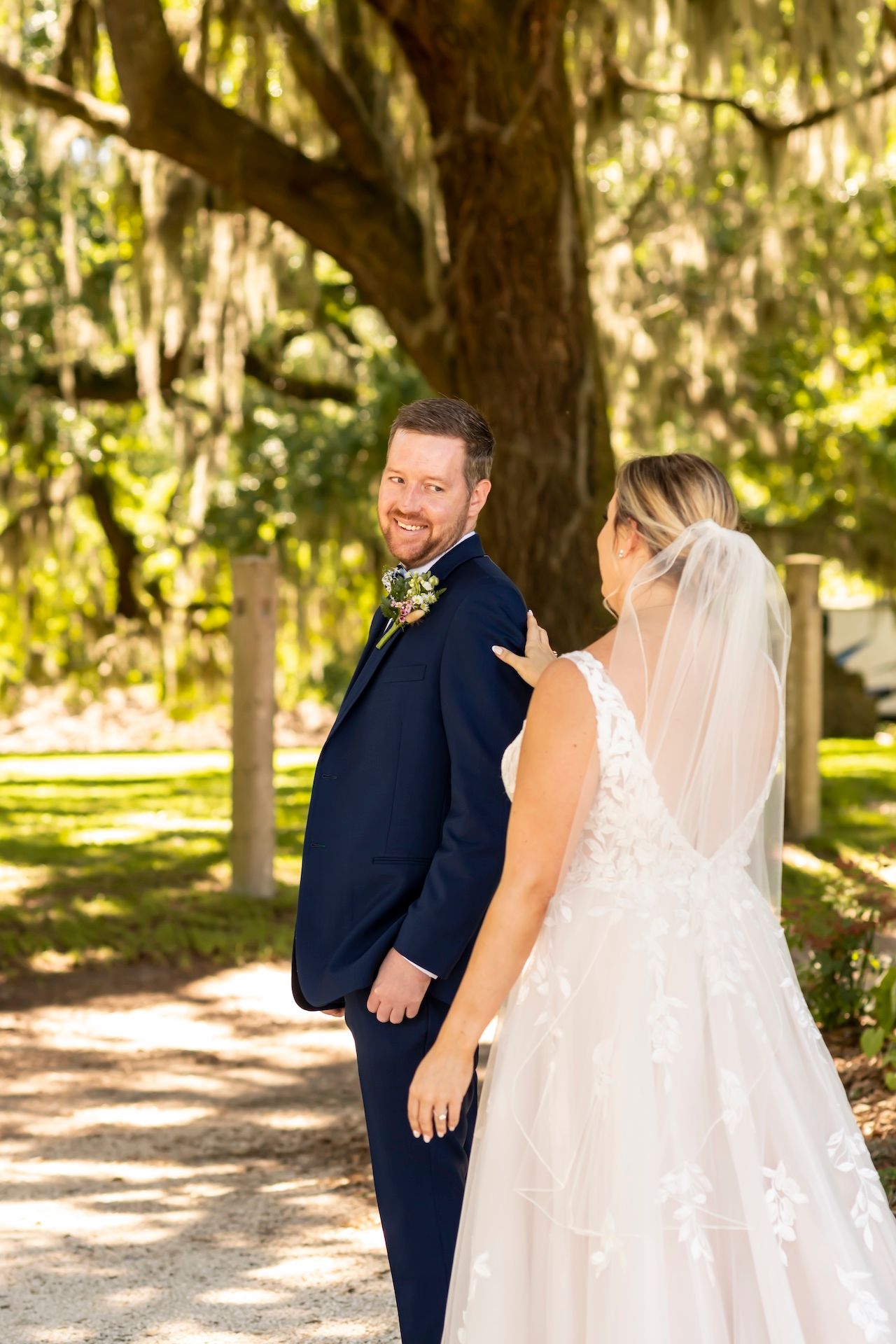 A couple shares a joyful first look moment under moss-draped oak trees at a scenic outdoor wedding venue.