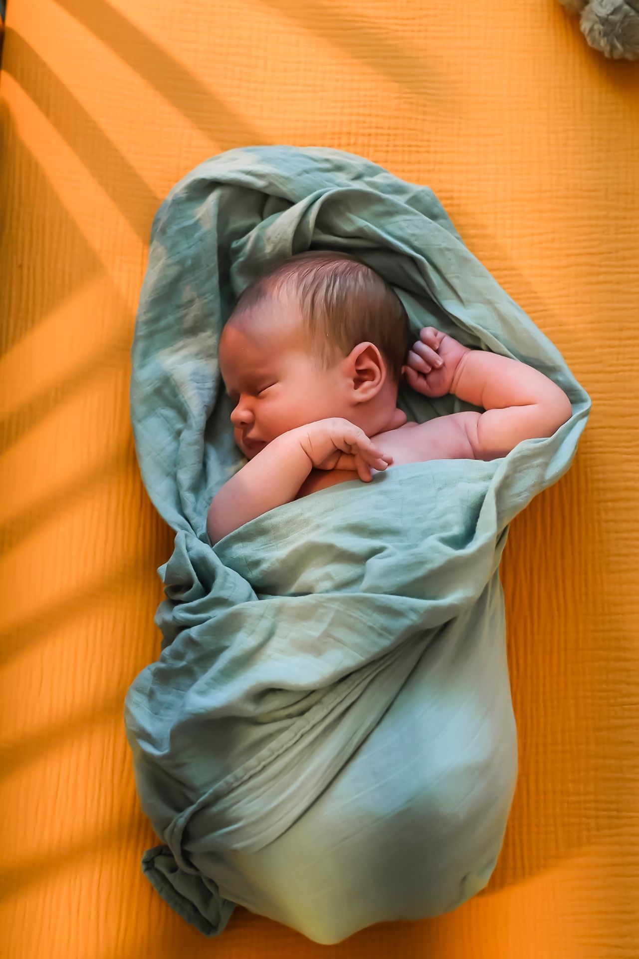 A peaceful sleeping newborn baby wrapped in soft turquoise fabric against an orange background.