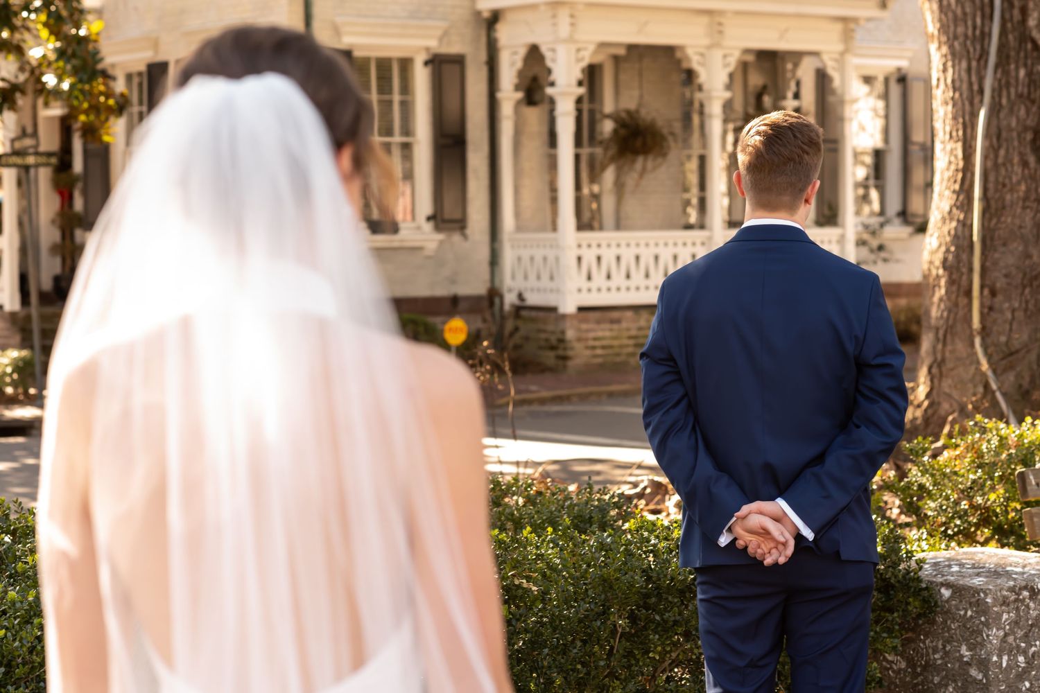 A wedding first look moment captured from behind, showing the couple outside a vintage Victorian house with ornate details.