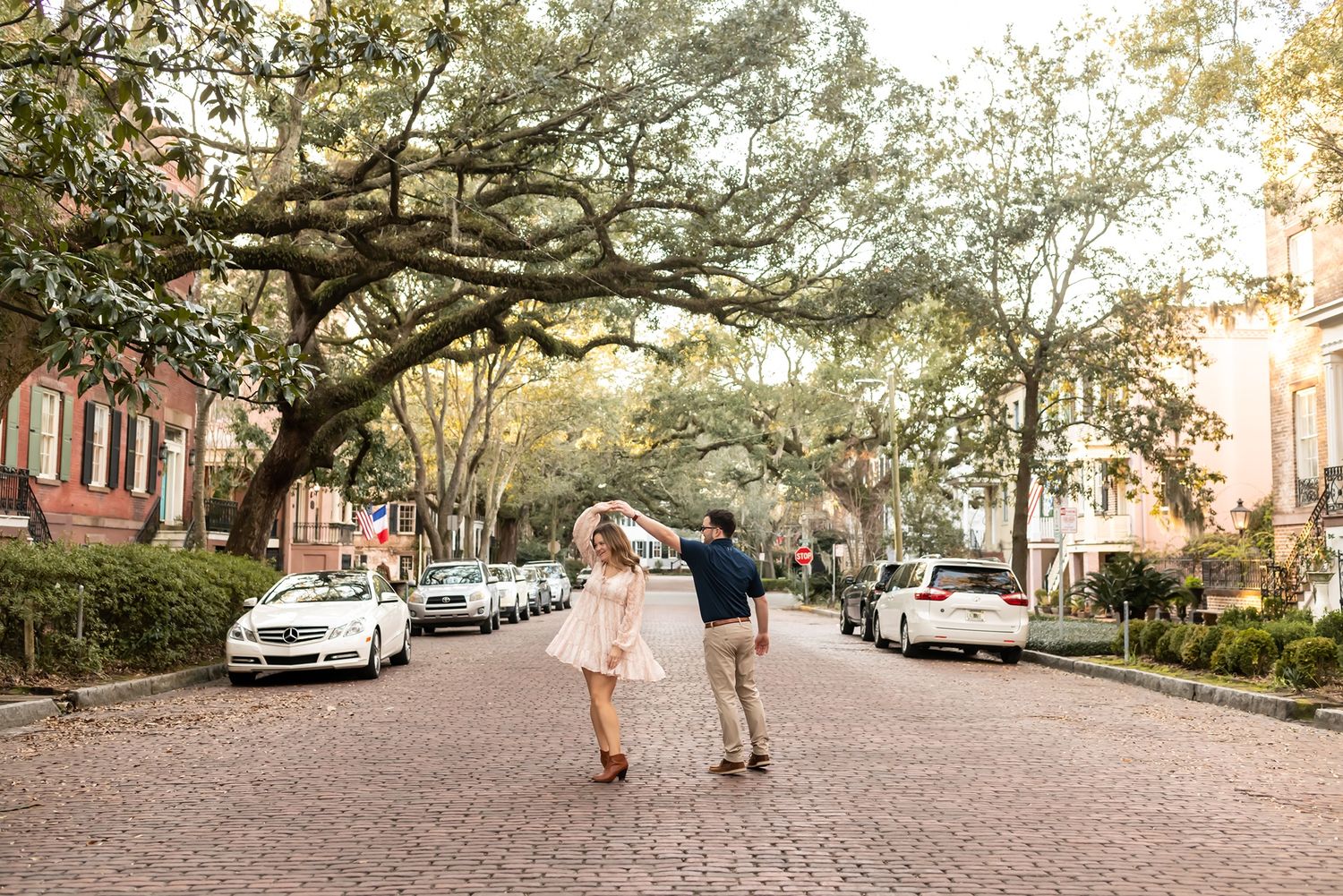 A couple walks down a romantic brick-paved street lined with oak trees and historic buildings in Savannah, Georgia.