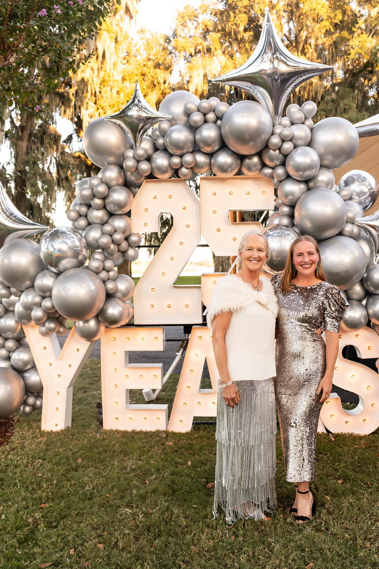 A glamorous silver balloon arch with 'YES' lettering creates a festive backdrop for an outdoor celebration.