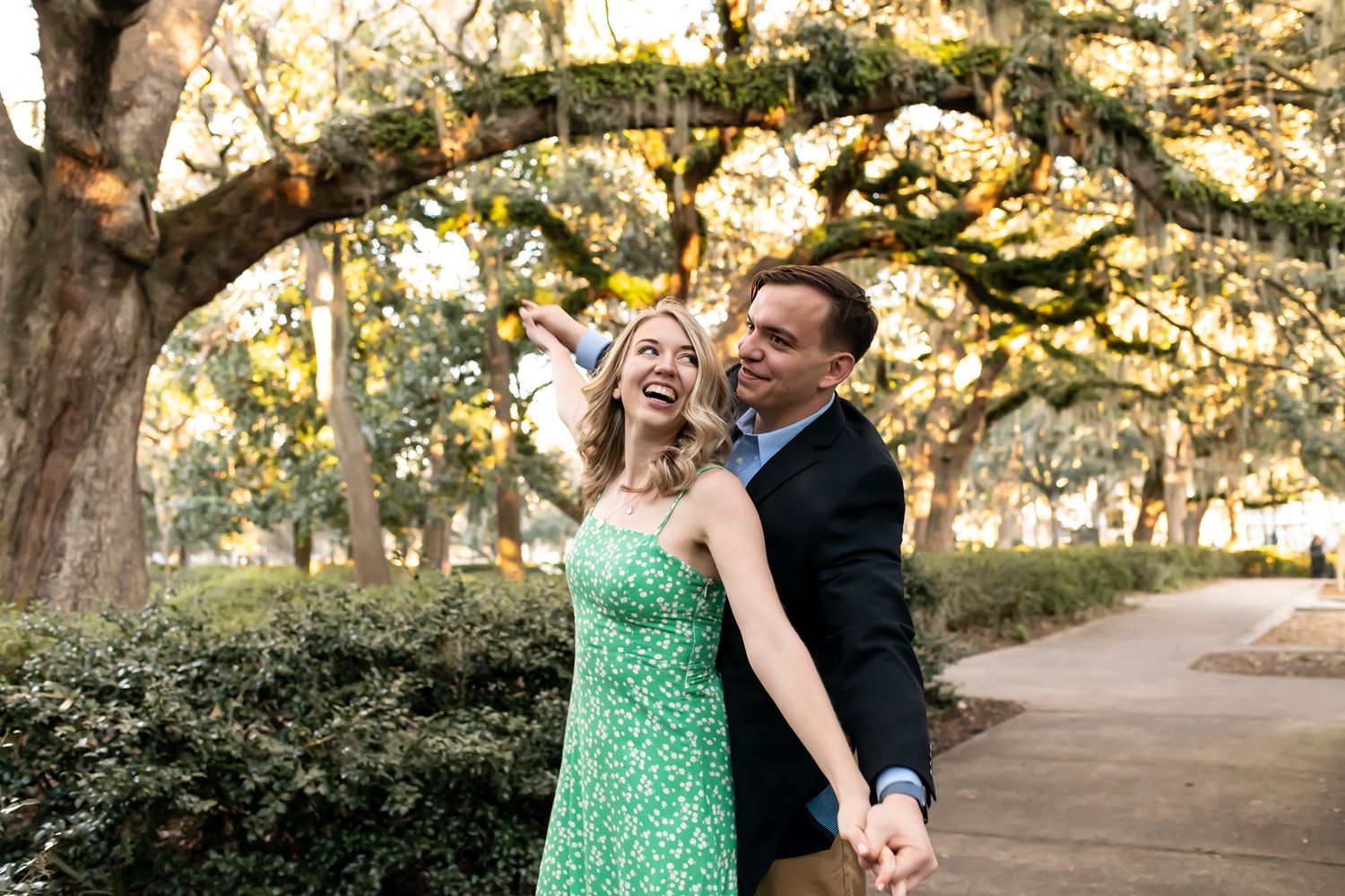 A couple dances together under large oak trees during sunset in a park setting.