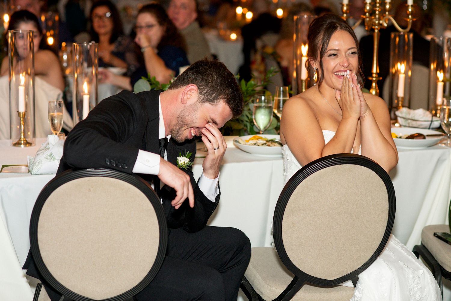 Wedding reception guests enjoy dancing and mingling around elegant white-clothed tables with candlelight.
