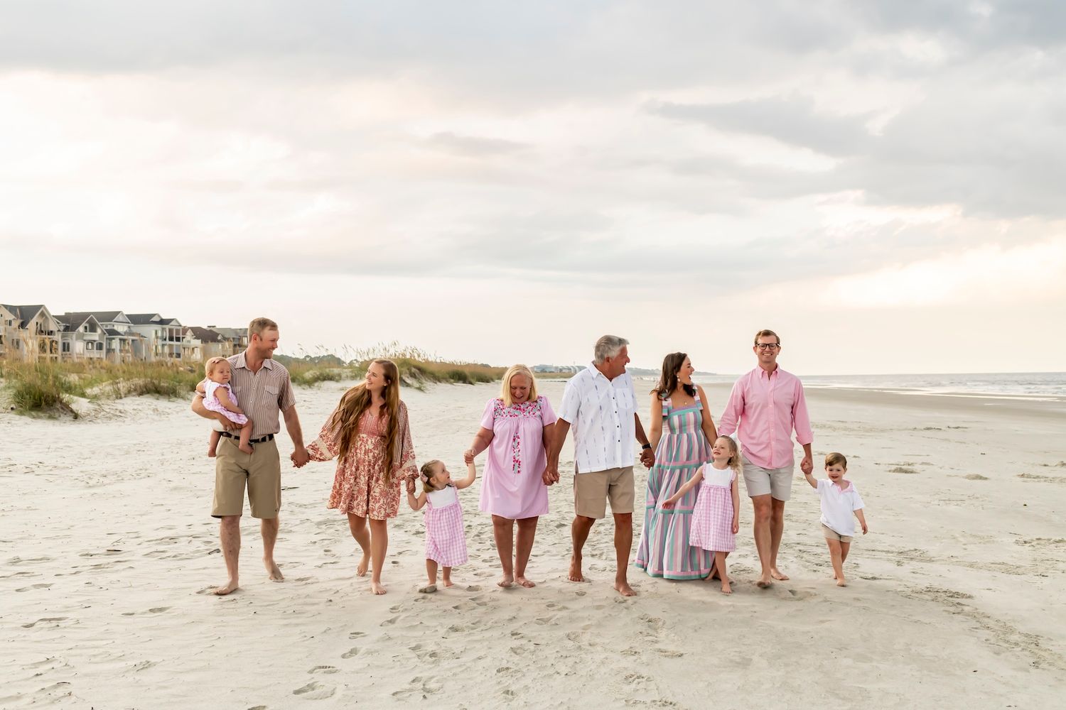 A family group walks together on a beach at sunset wearing coordinating pink and neutral coastal outfits.