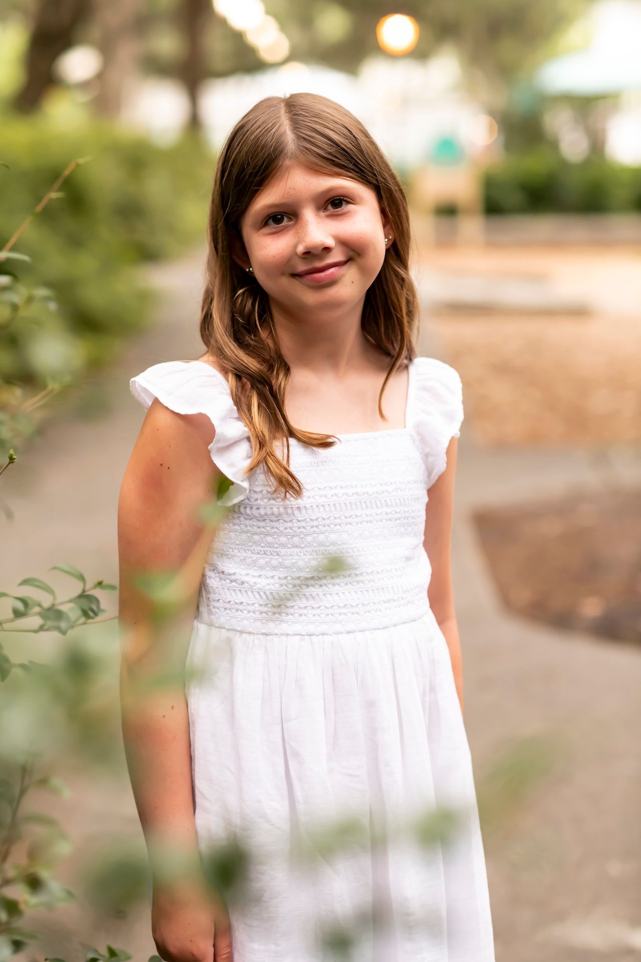 A young person in a white summer dress stands in a garden with soft natural lighting.