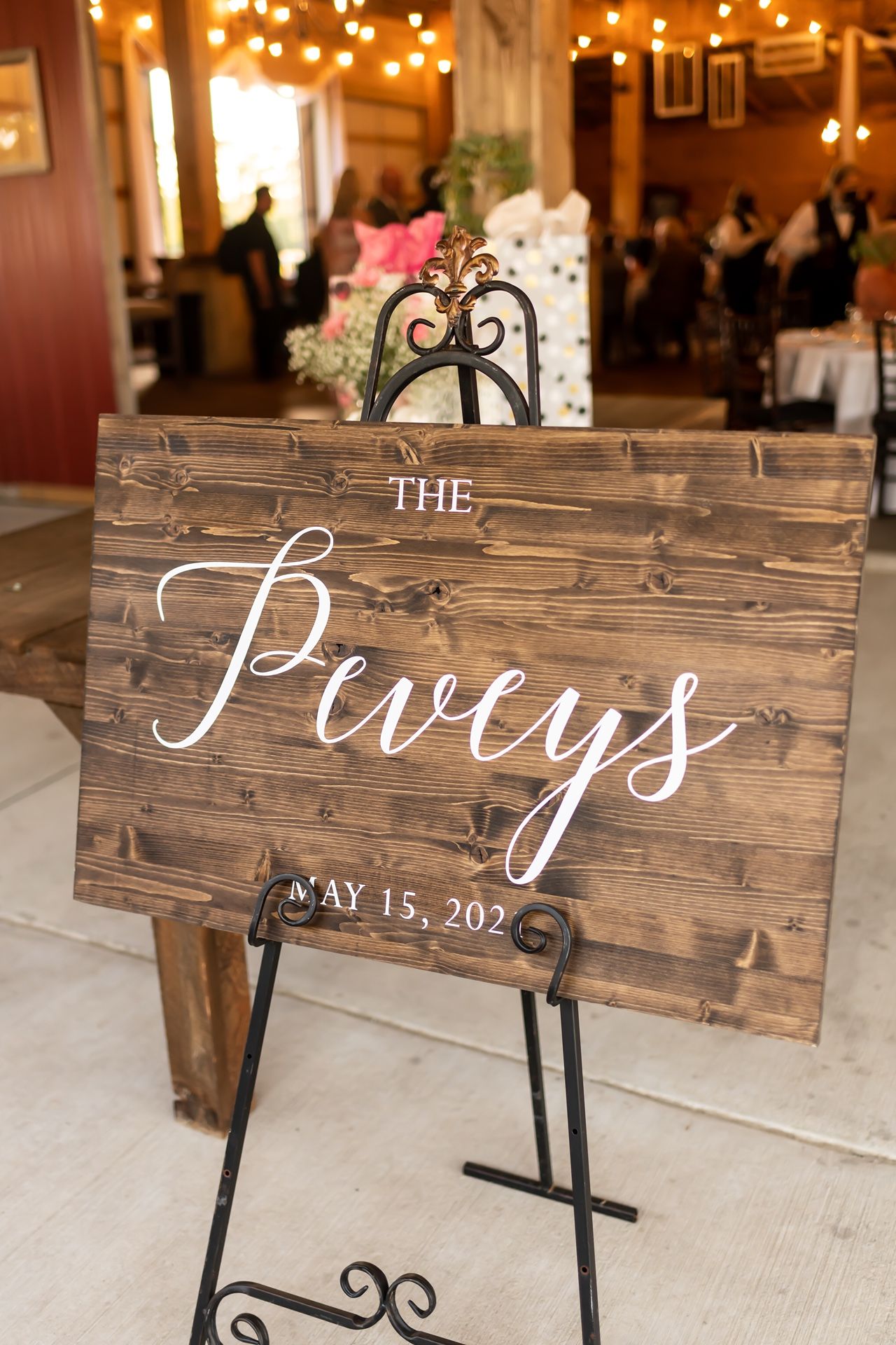 Rustic wooden wedding sign boards on black metal stands displaying elegant white calligraphy text in a ballroom setting.