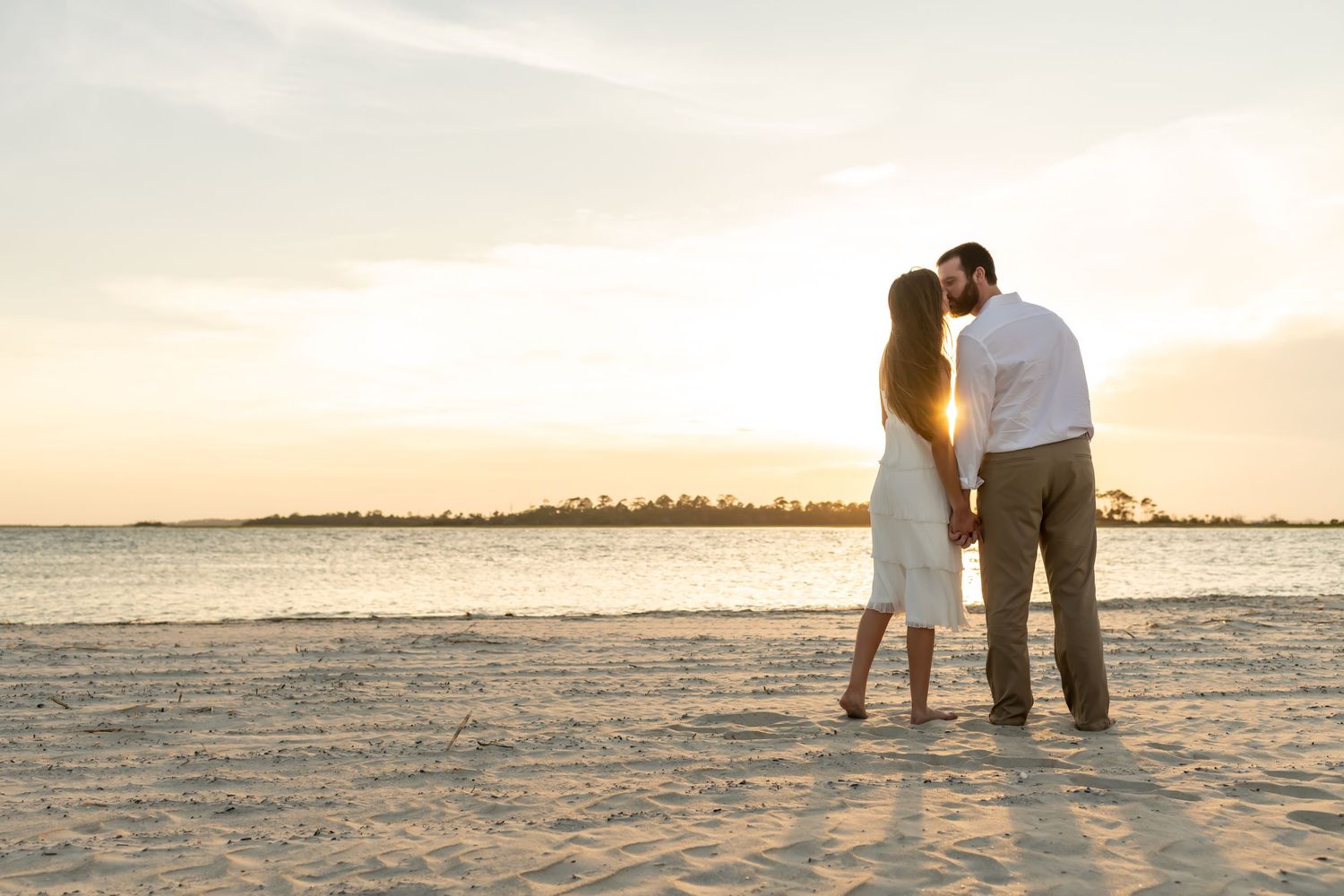 Romantic silhouette of a couple standing together on a sandy beach during a golden sunset over the ocean.