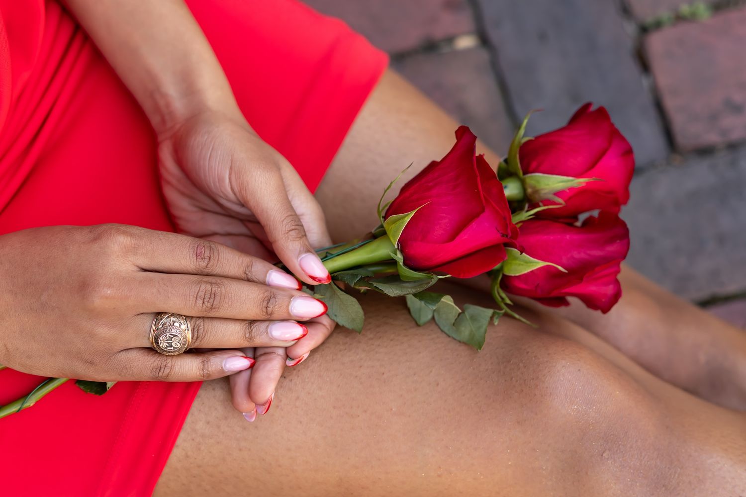 Hands holding red roses while wearing a red dress and white manicure with an engagement ring on display.