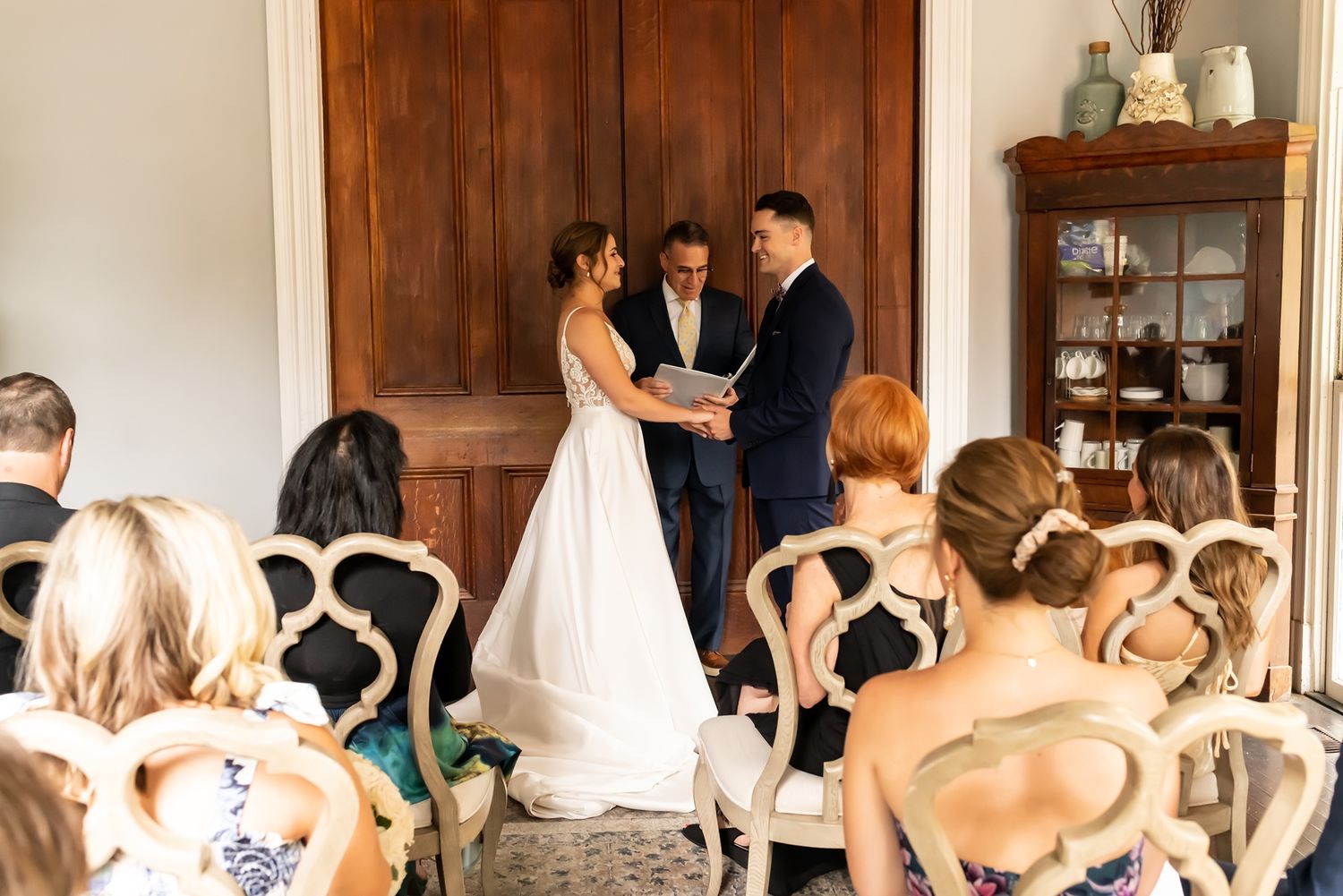 Wedding ceremony in a bright indoor venue with elegant chairs and wooden door panels.