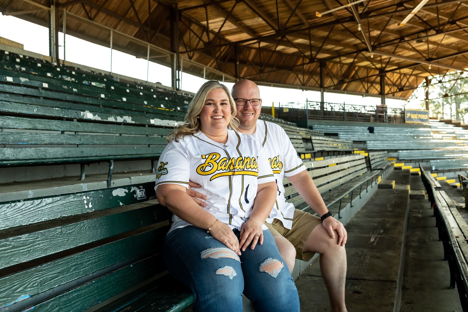 Two people sit together on green bleachers in an empty stadium wearing matching white t-shirts.