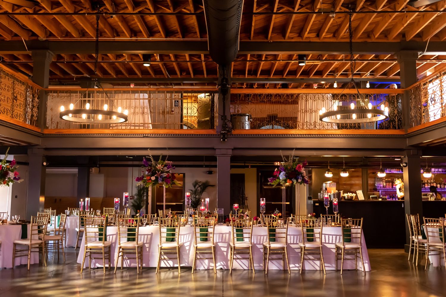 Elegant wedding reception venue with exposed wooden beams, banquet tables, and warm lighting in a rustic industrial space.