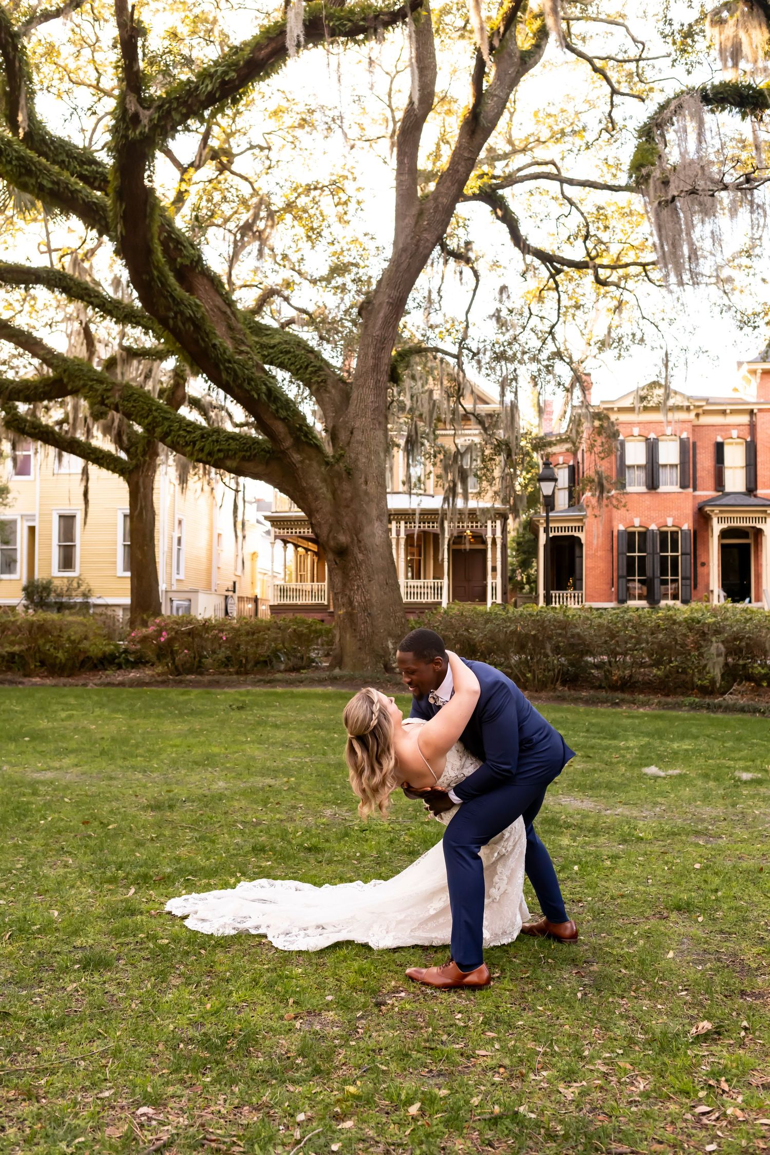 A couple dips romantically beneath a sprawling oak tree draped with Spanish moss in a historic Southern square.
