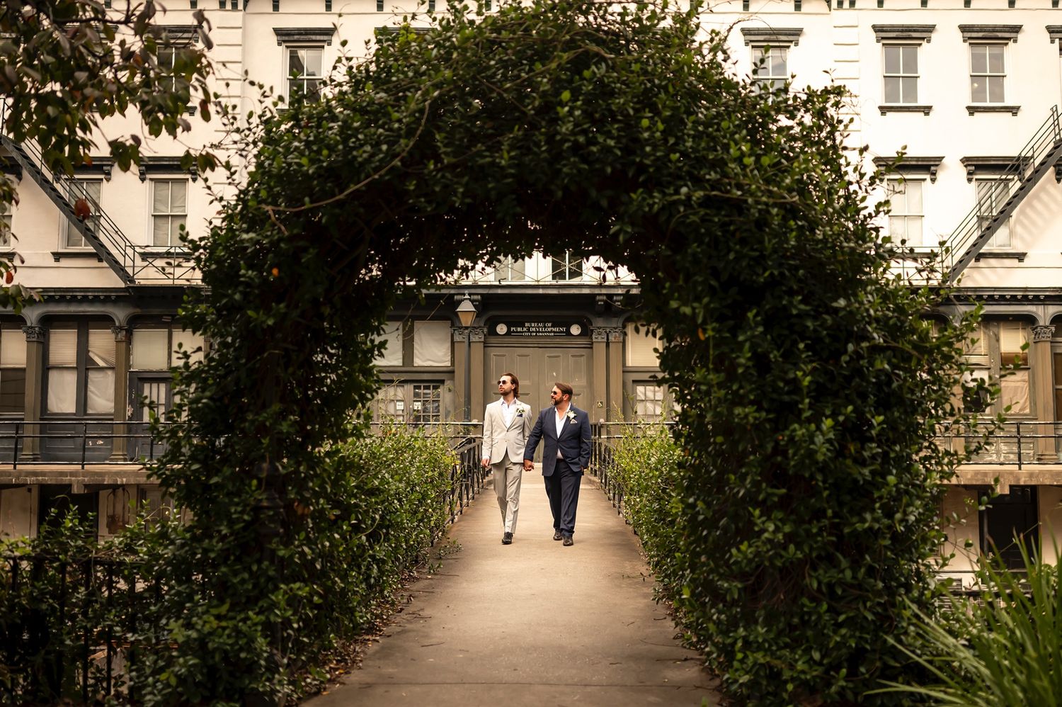 A garden archway covered in lush greenery creates a romantic pathway in front of a historic building.