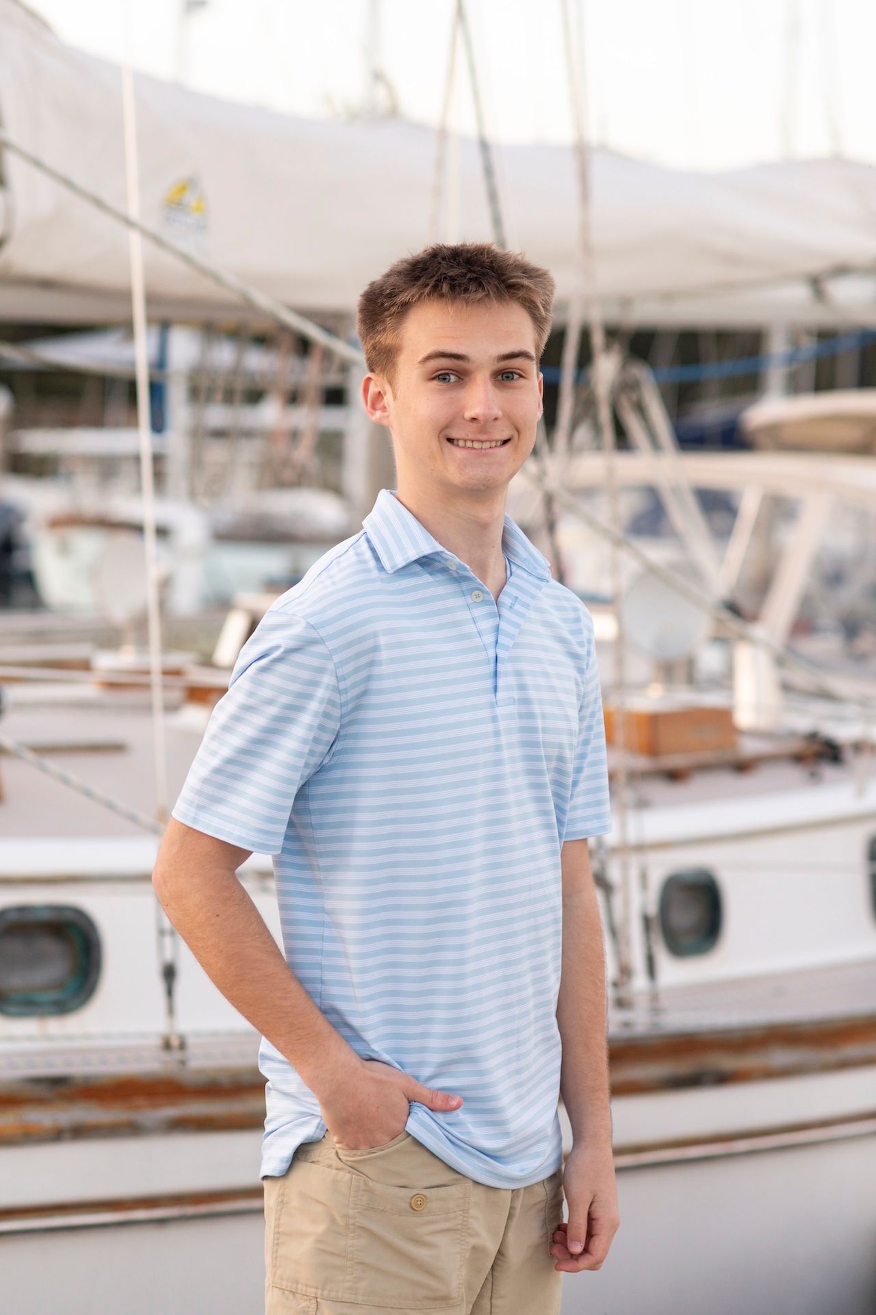 Senior boys poses in front of a sail boat at Isle of Hope Marina for his senior portraits.