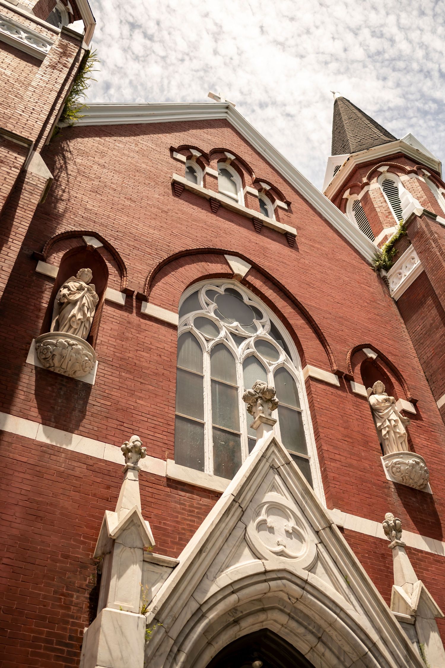 Gothic revival church facade with red brick walls, ornate arched windows, and decorative stone statues along the exterior.