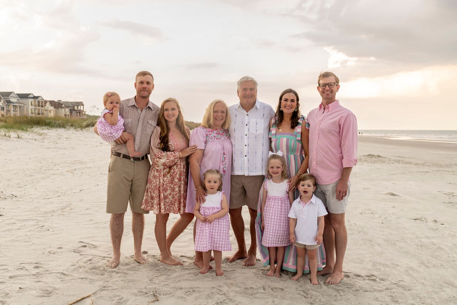 A group of people wearing coordinating beach outfits pose together on a sandy beach at sunset.